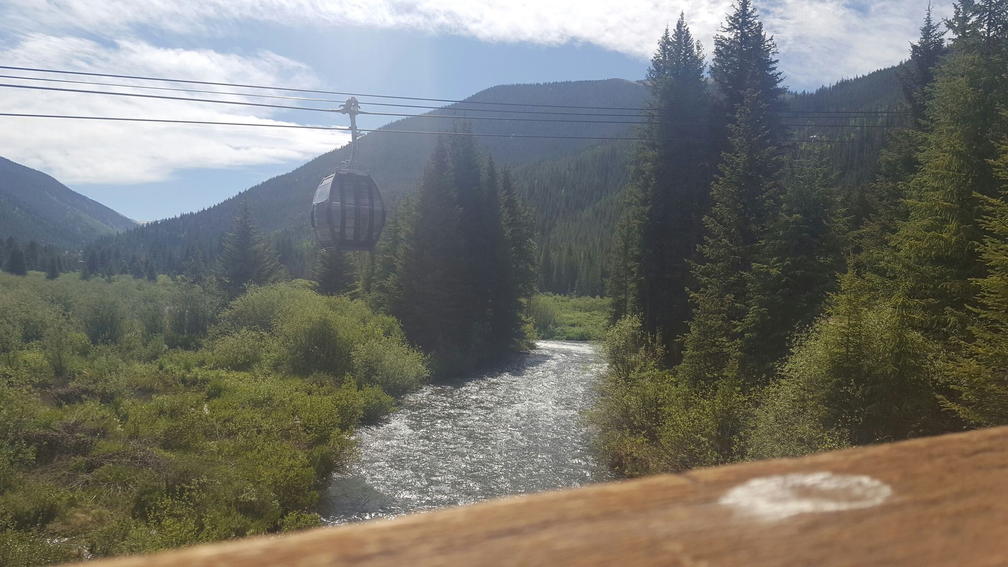 Gondola car moving over a sparkling river in a green mountain valley. - Girl Scouts to Let It Ride Loop