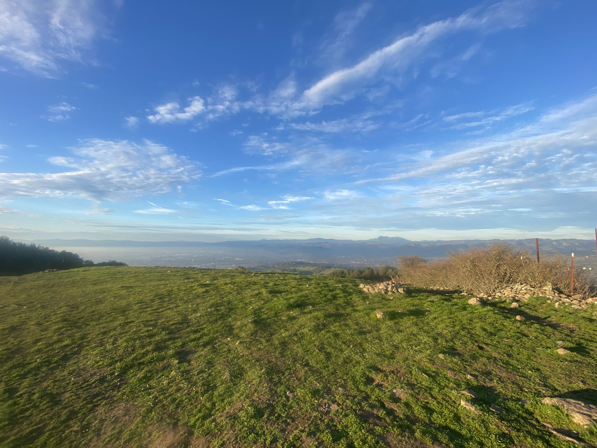 Bright green hillside overlooks a hazy valley under a blue, cloudy sky. - Taylor Mountain via Western Route