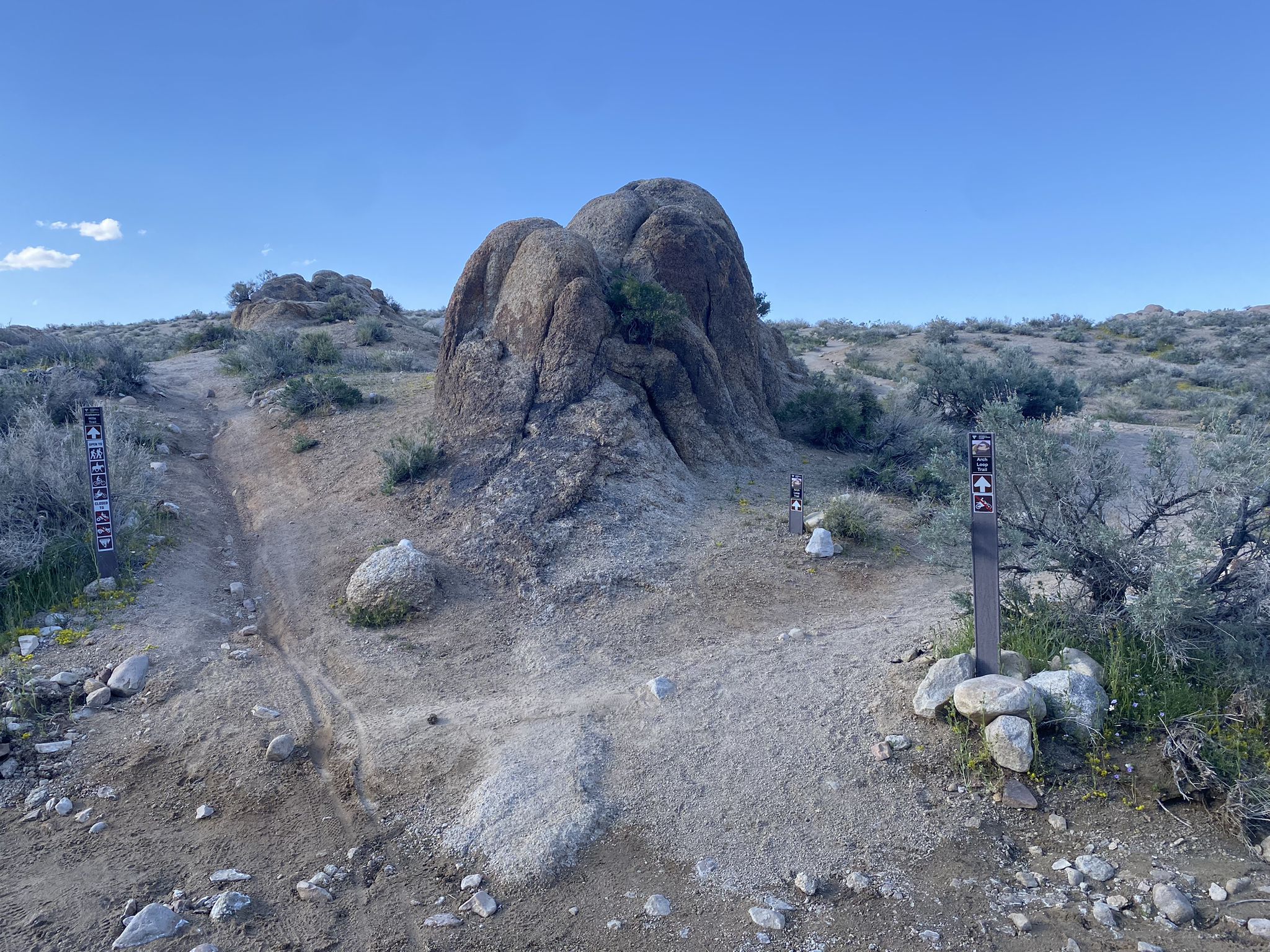 Dirt trail forks around large rock formation under clear blue sky. - Alabama Hills loop