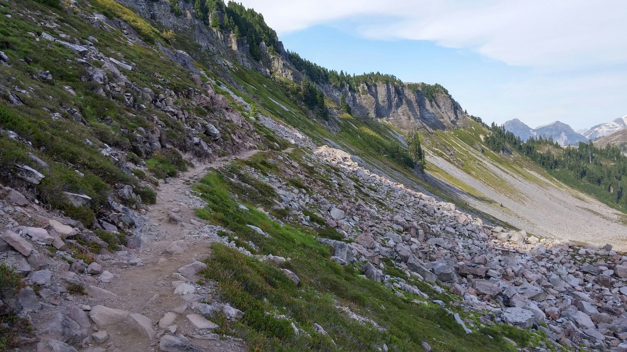 Rocky trail traversing a steep, green mountain slope with cliffs above. - Artist Point – Chain Lakes Trail loop from Artist Point Trailhead