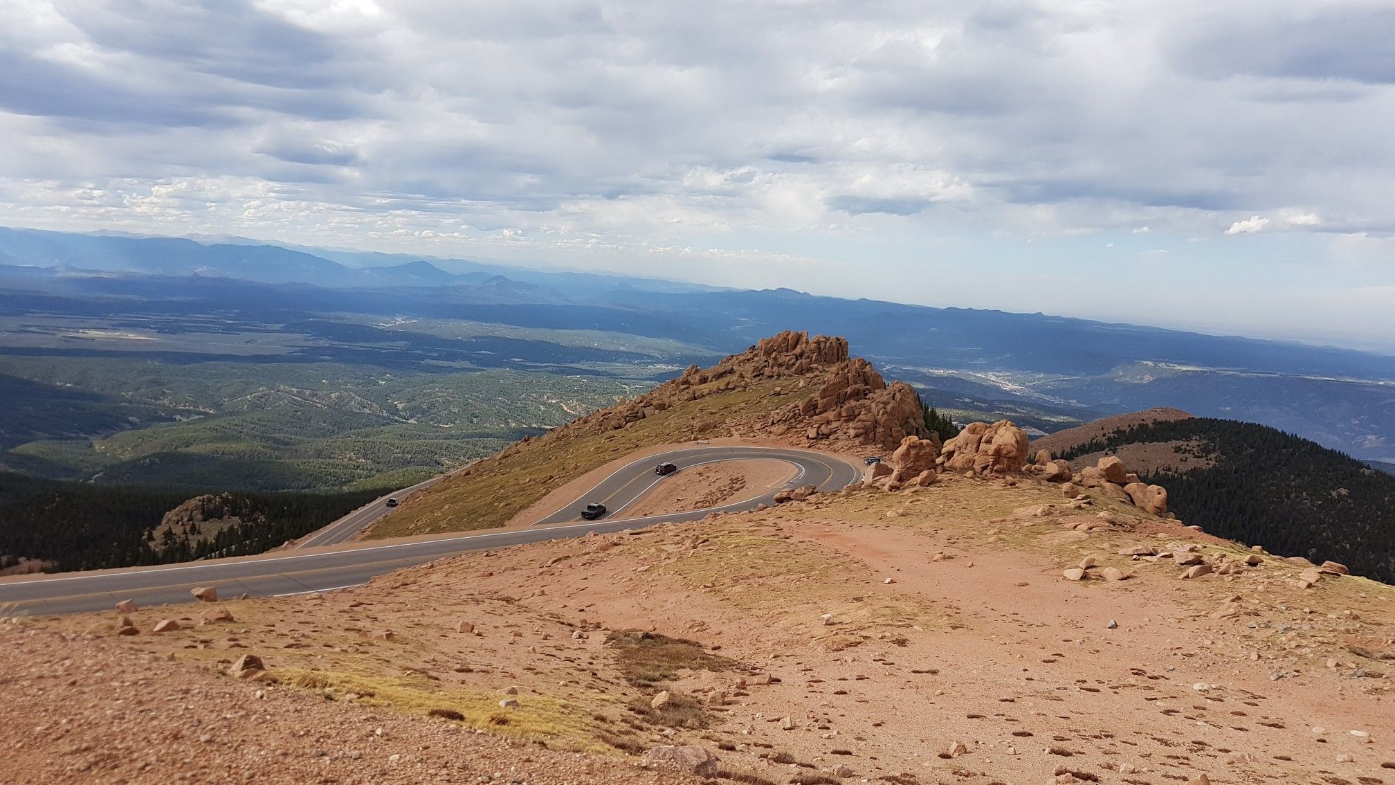 Winding mountain road with cars, vast landscape under cloudy sky. - Pikes Peak Highway: Cascade to the Summit of Pikes Peak