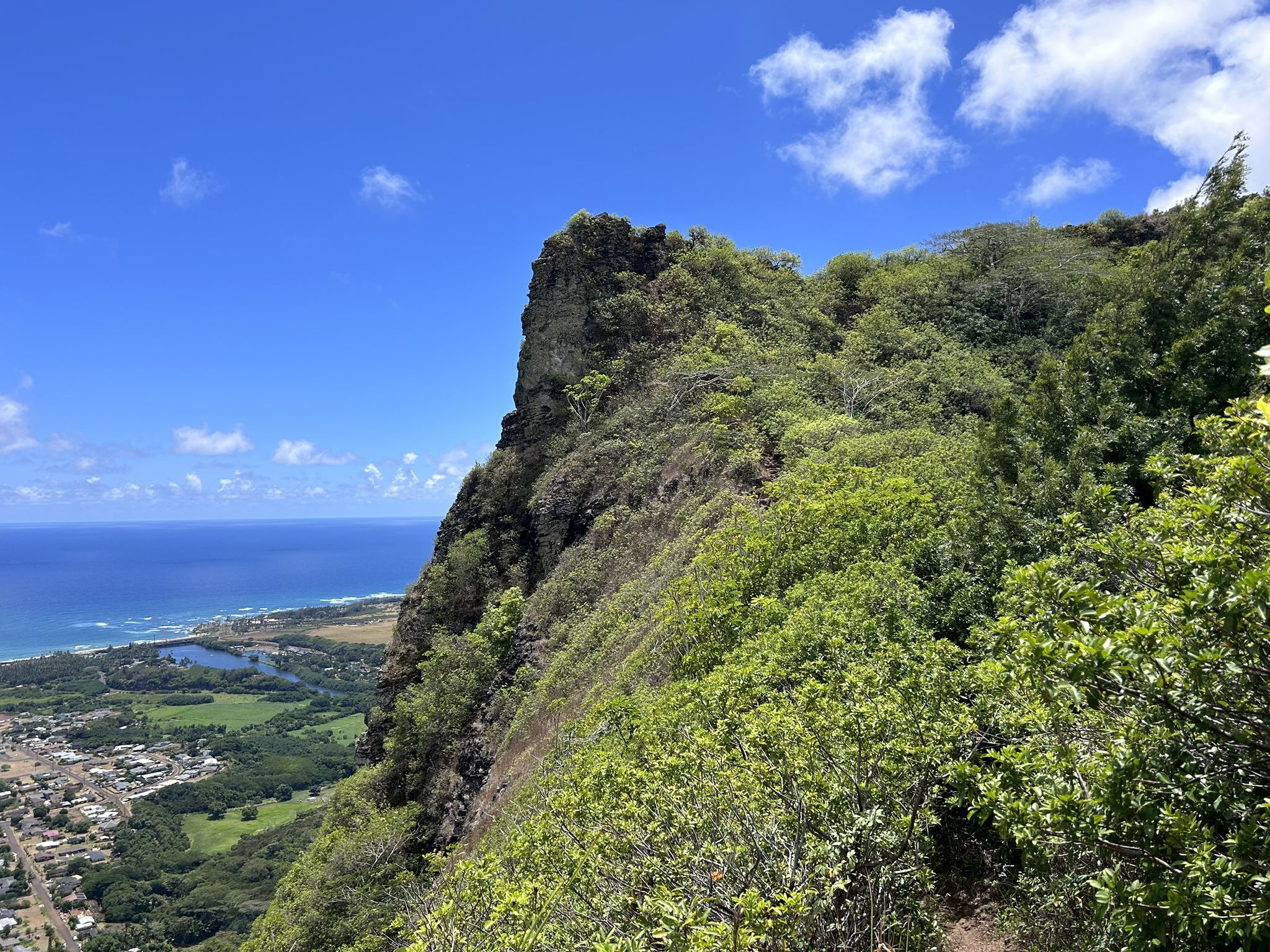 Steep green mountain cliff overlooking a bright blue ocean and coastal town. - Waipouli Beach Park to to Makaleha Falls trailhead