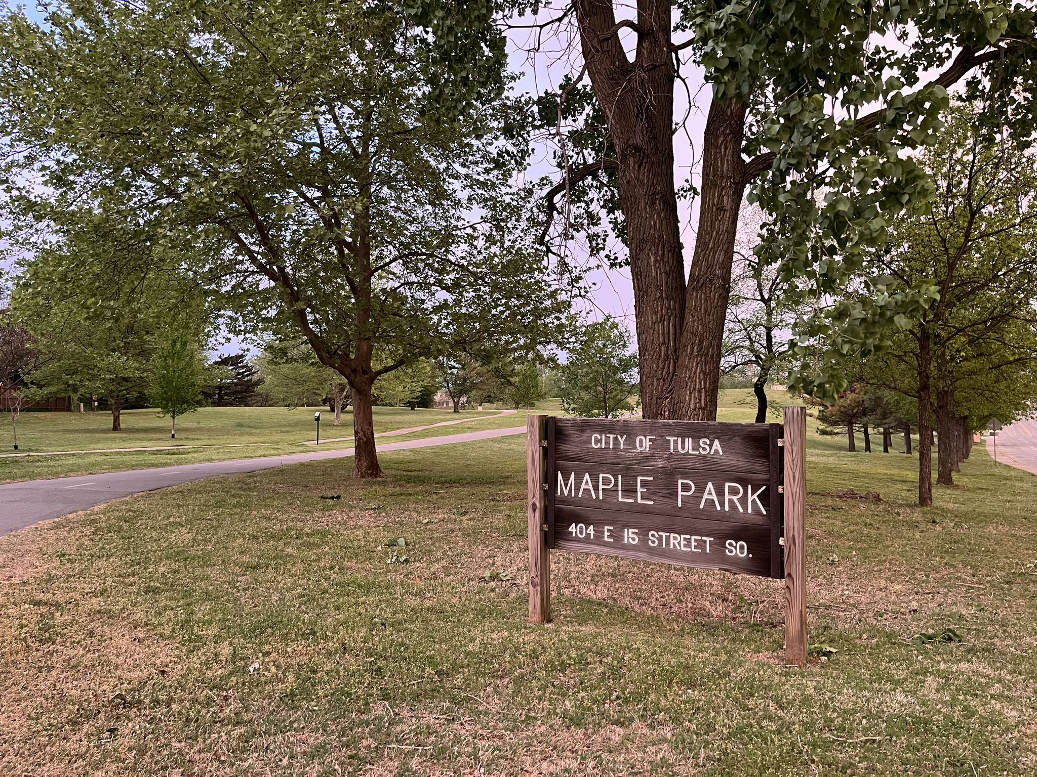 Wooden sign in a grassy park with large trees and a paved path. - Tuckabache and River Parks East Bank Trail Loop