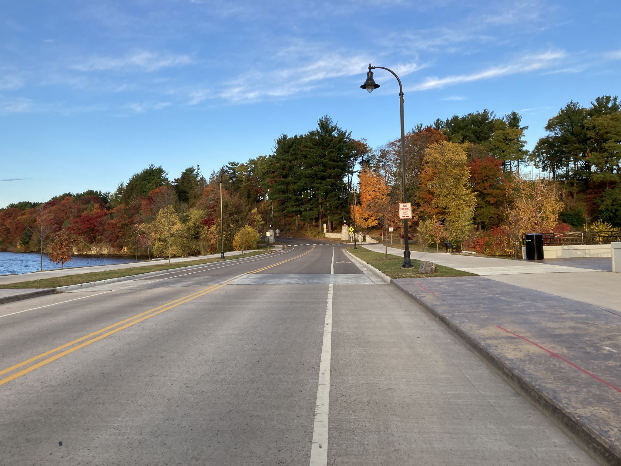 Empty road and sidewalk beside a lake with colorful autumn foliage. - Lakeshore Trail loop from Carson Park