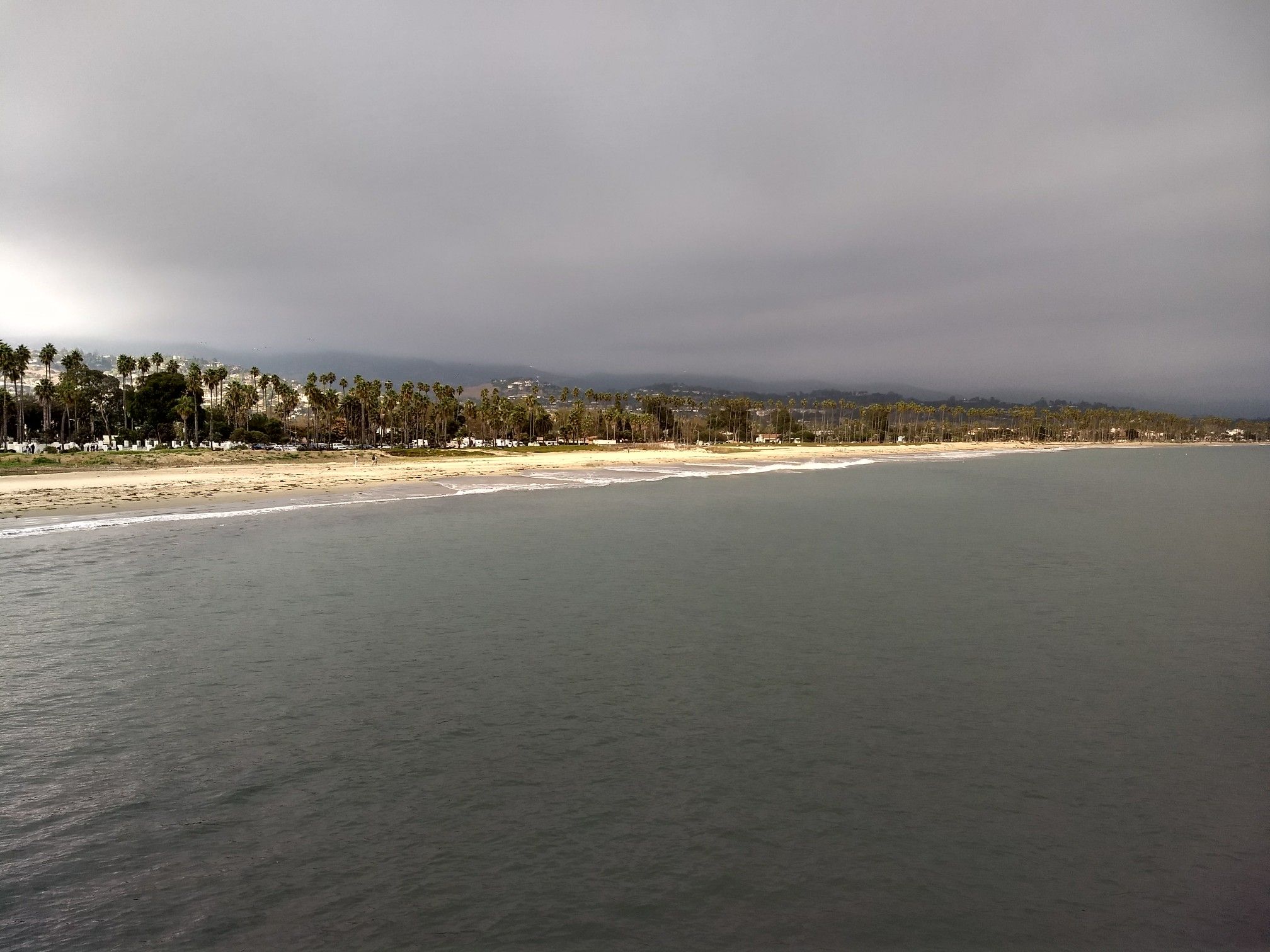 Dark ocean, sandy beach, and tree-lined coast under a cloudy sky. - La Cumbre Peak – Stearns Wharf ⛵ Santa Barbara loop from Santa Barbara
