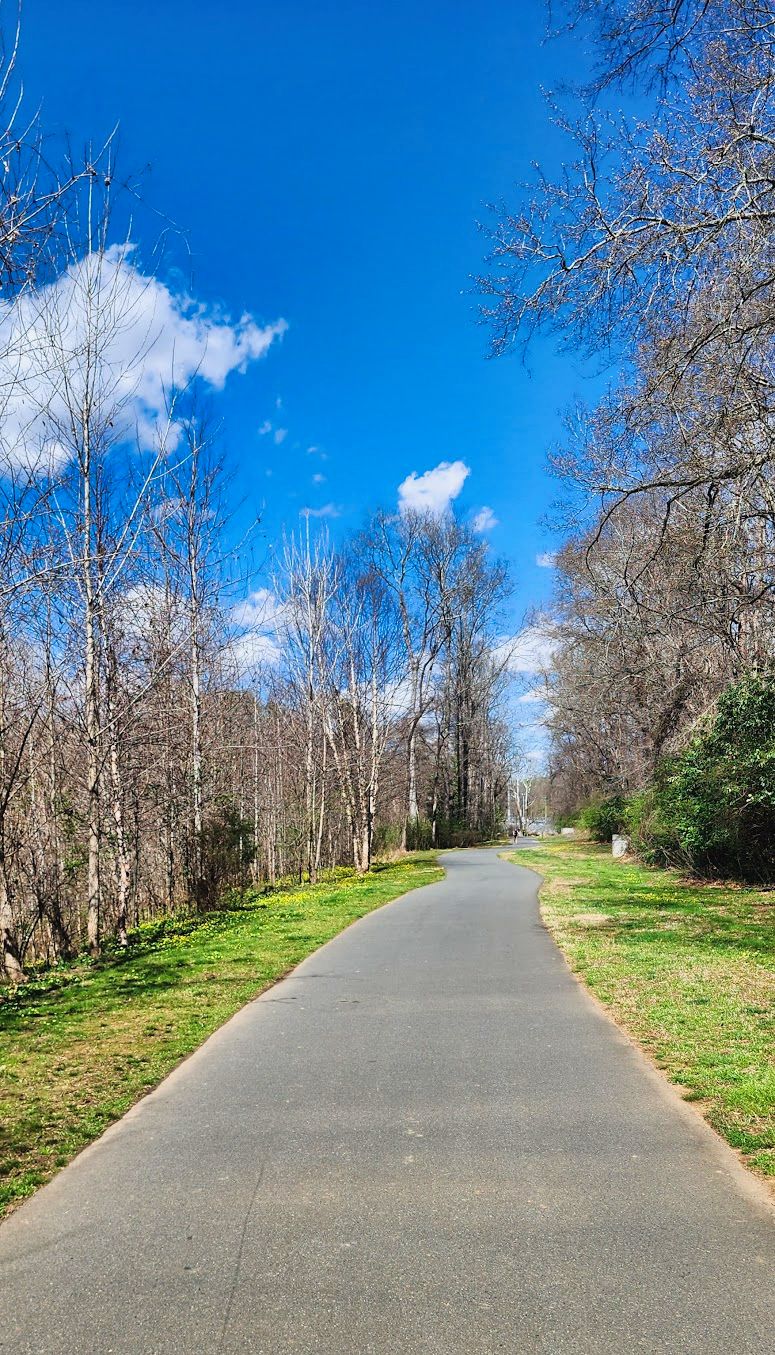 Paved path through a park with bare trees under a bright blue sky. - Huntingtowne Farms Park loop from Ajewia Lake