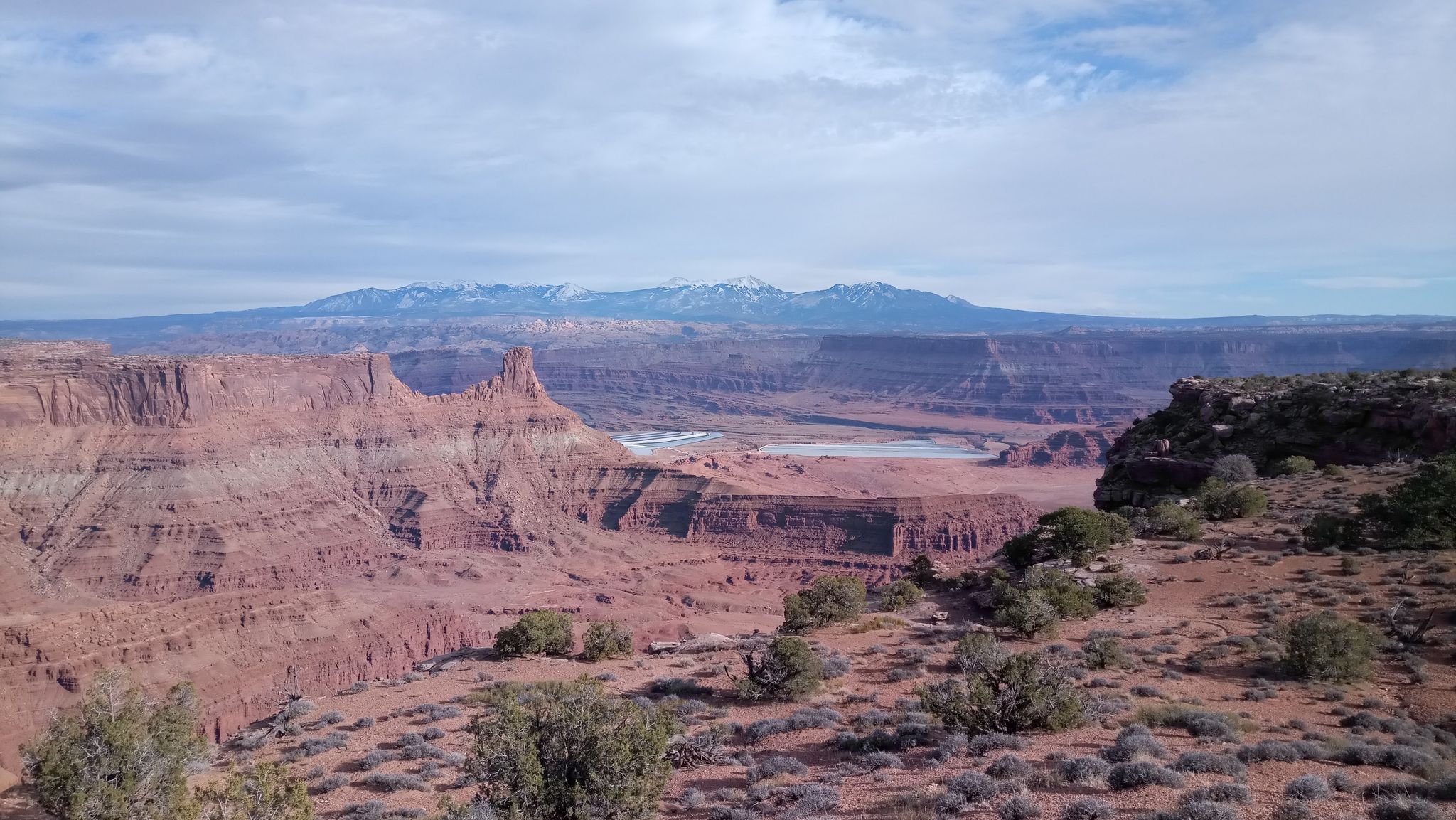 Vast desert canyon with distant snow-capped mountains under a partly cloudy sky. - East and West Rim Loop