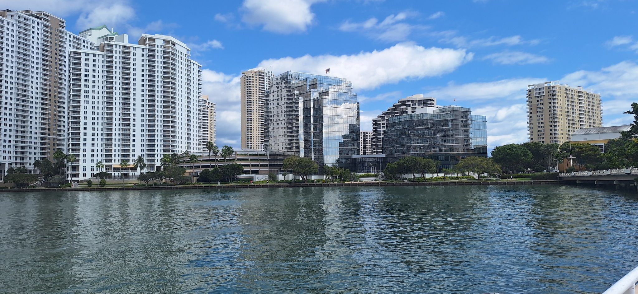 City skyline with tall buildings and water under a bright, cloudy sky. - Brickell Key Loop