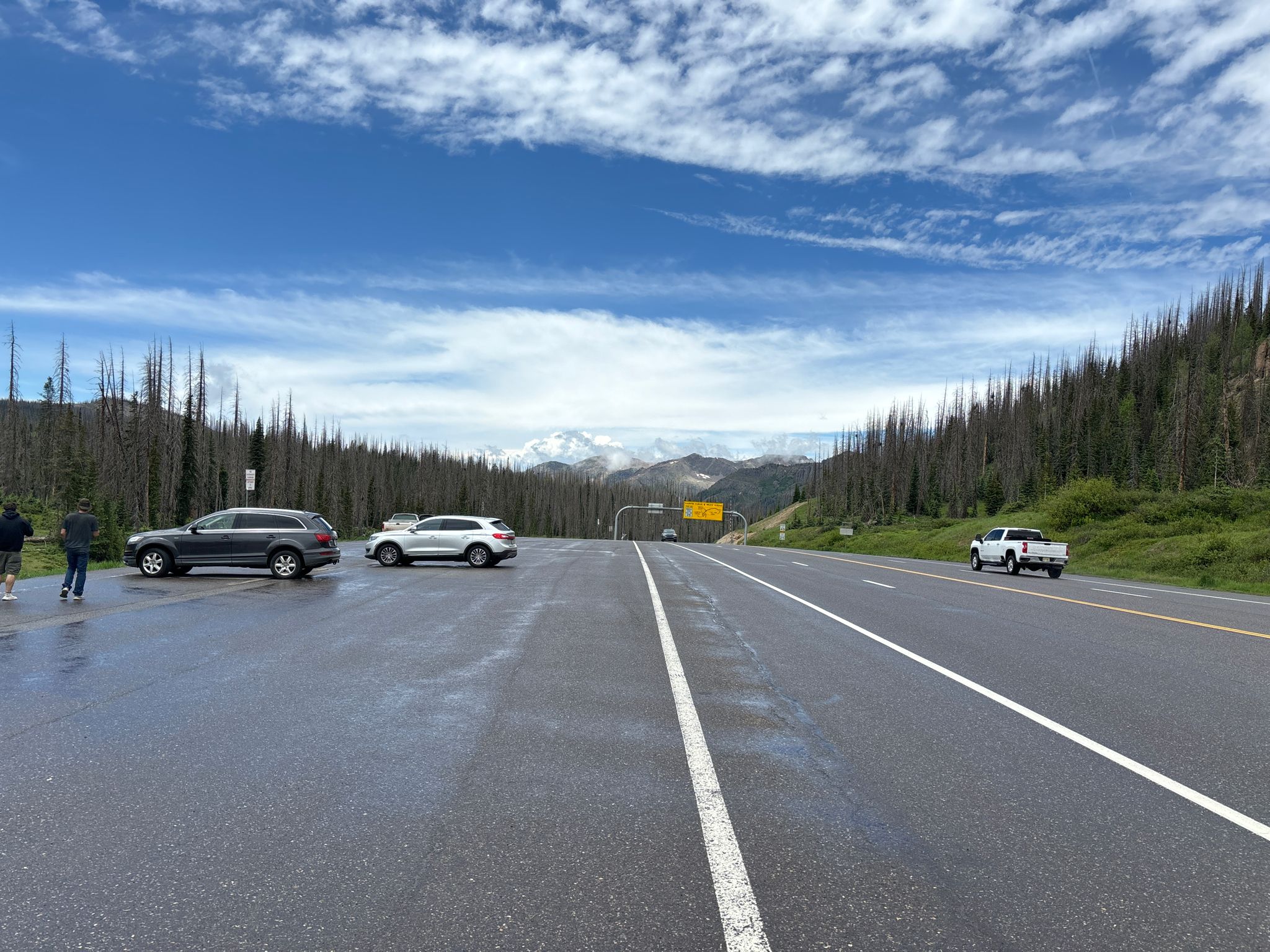 Cars parked on a wide road, with distant mountains under a cloudy sky. - Alberta Peak via Continental Divide National Scenic Trail
