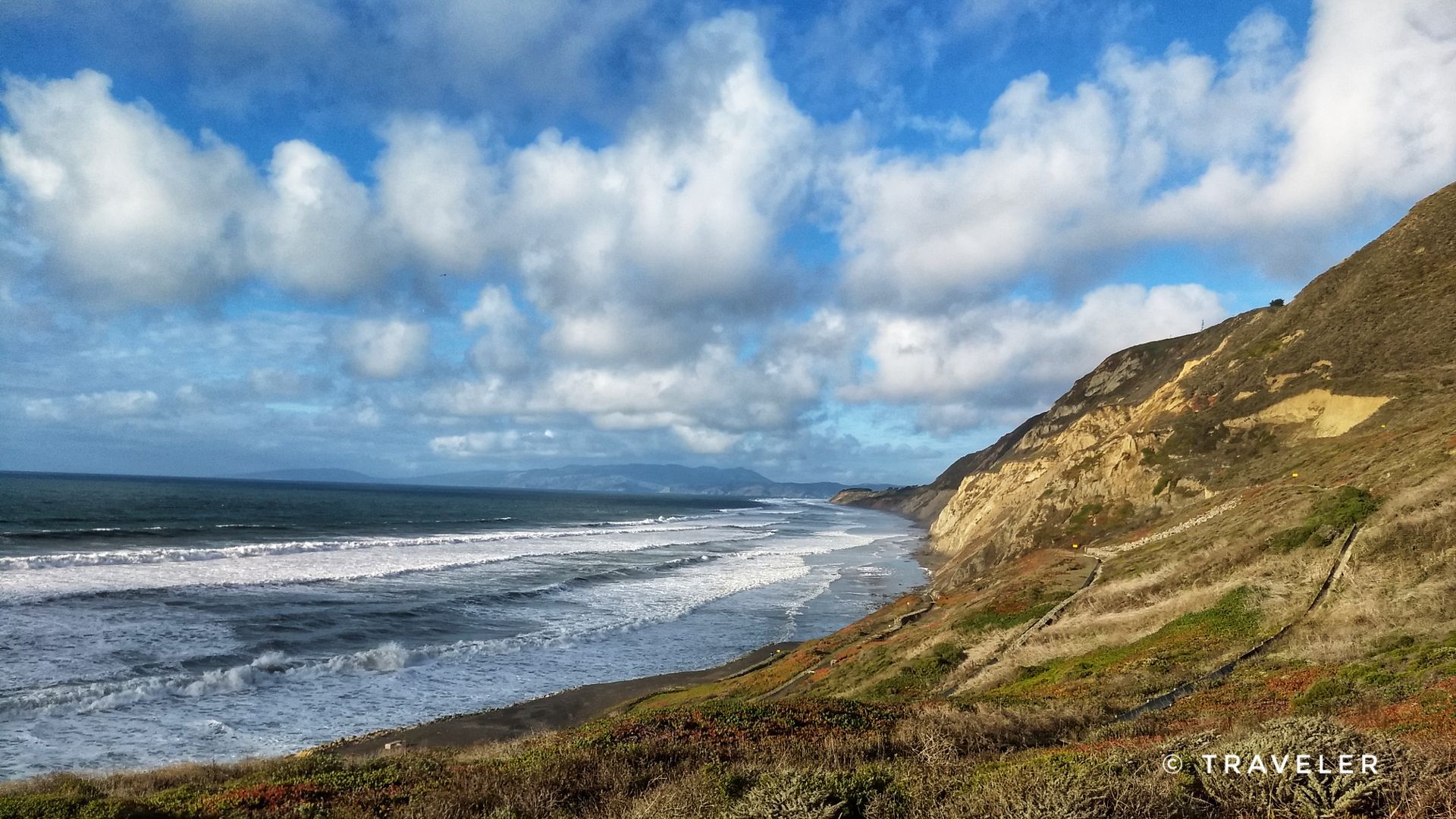 Bright coastal view with ocean waves, a rugged hillside, and blue sky. - Mussel Rock Trail
