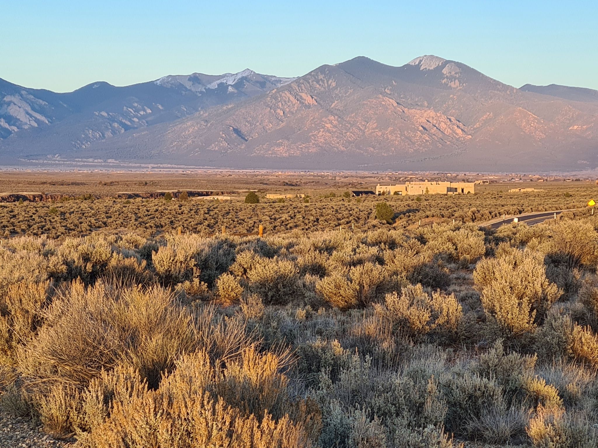Wide desert landscape with sagebrush, distant buildings, and large mountains. - Rift Valley Loop Trails