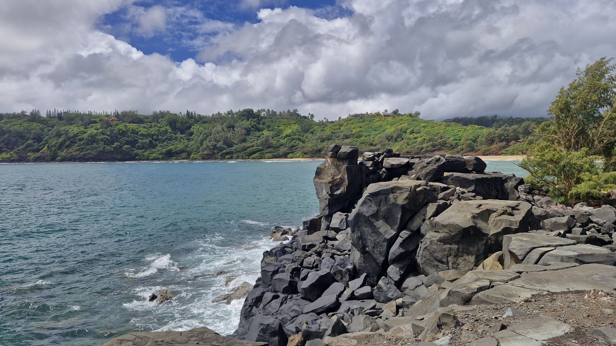 Rugged dark rock formations meet blue ocean under a partly cloudy sky. - Mokolea Point Trail