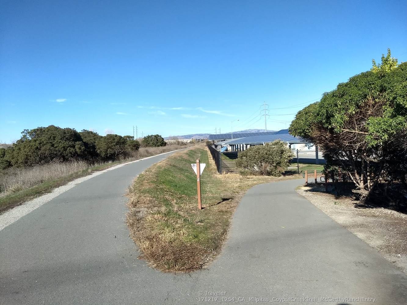 Paved trail forks, passing solar panels under a clear blue sky. - Coyote Creek Trail