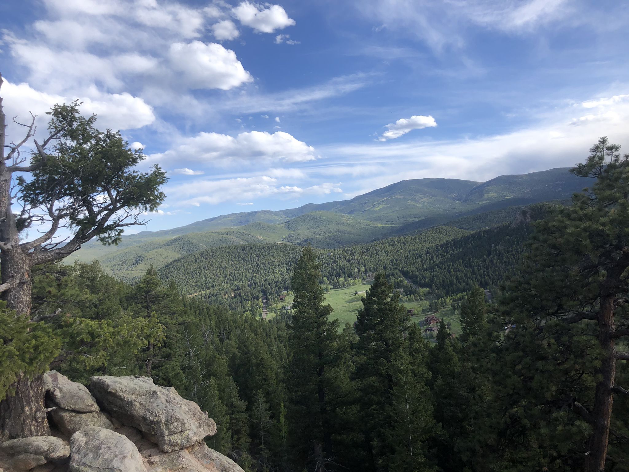 Rocky foreground overlooking a vast green forest and distant mountains. - Evergreen Mountain Summit Loop