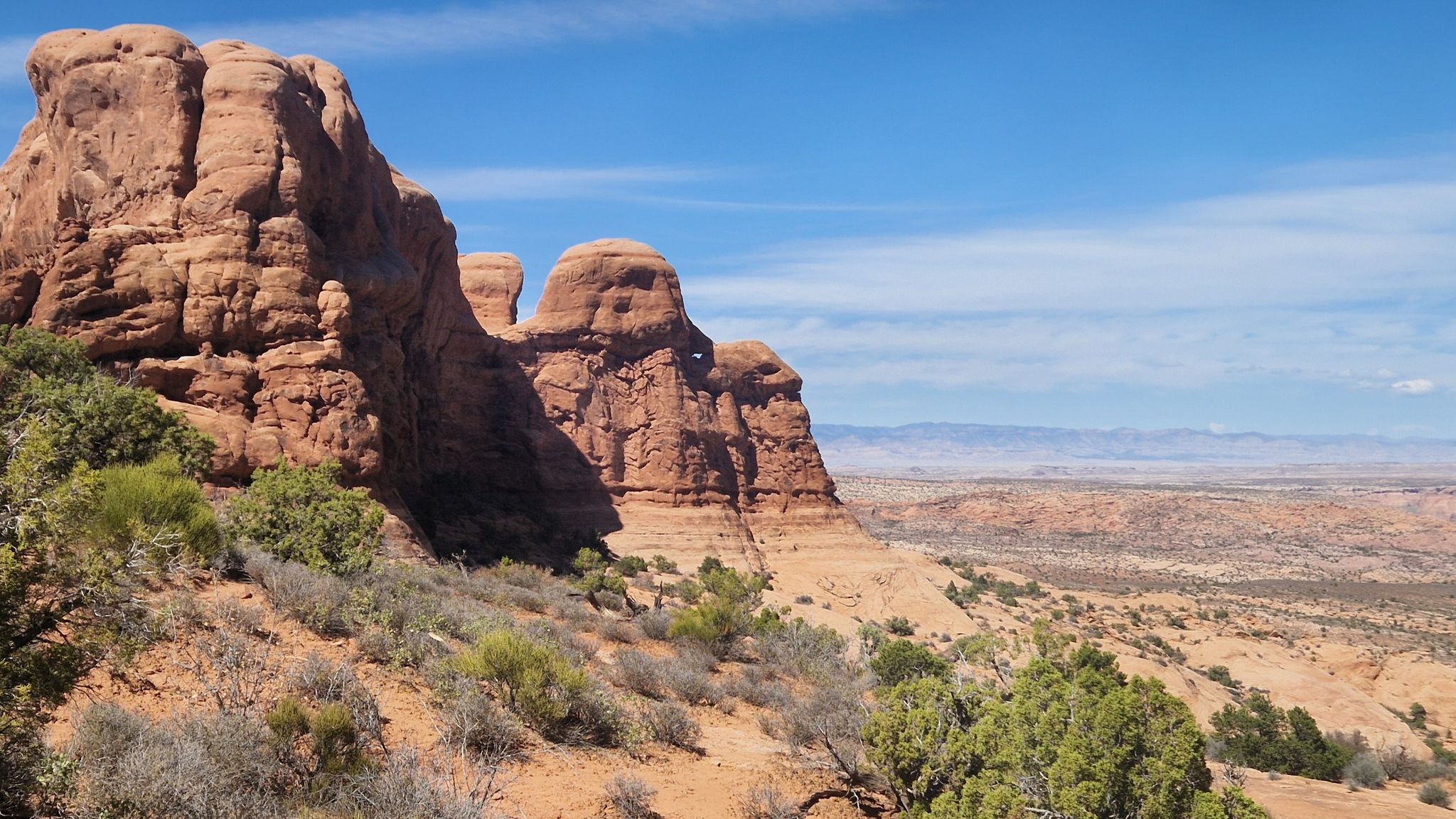 Red rock formations under a bright blue sky, overlooking a vast desert. - Windows Loop Trail