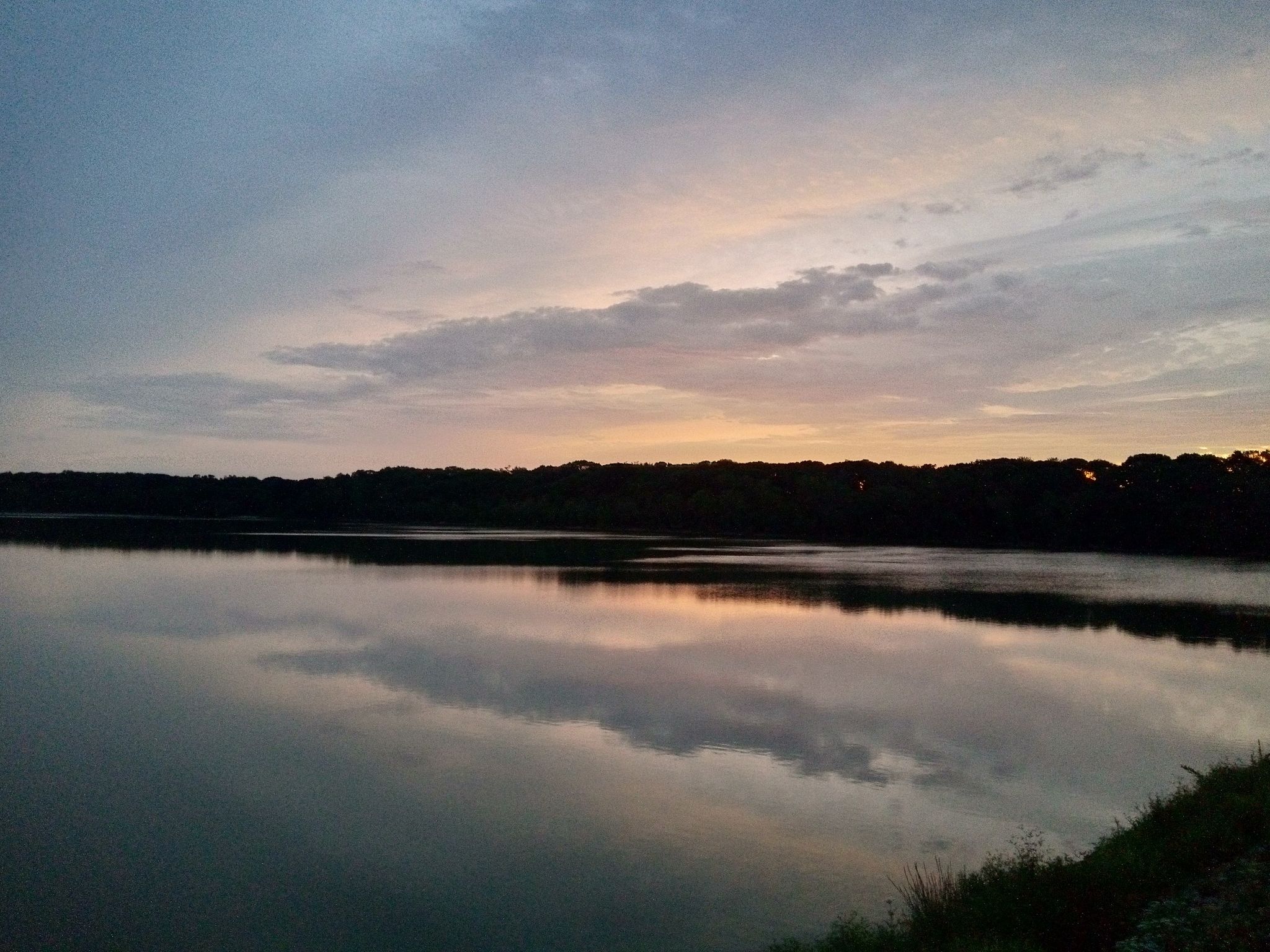 Serene lake at dusk, reflecting cloudy sky and distant treeline. - Hempstead Lake Bridle Trail