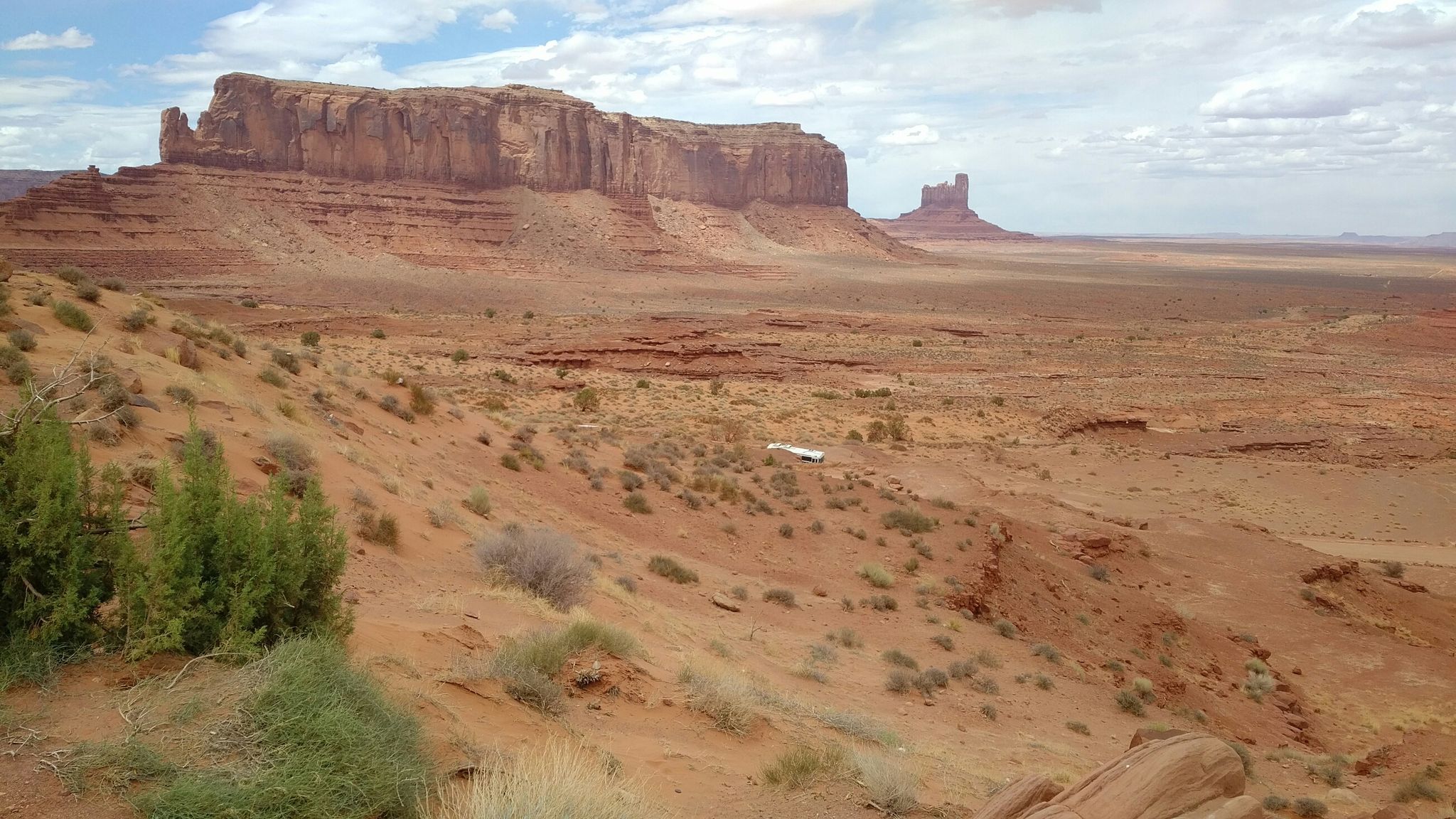 Wide desert landscape with large red rock mesas and sparse vegetation under a cloudy sky. - Wildcat Trail
