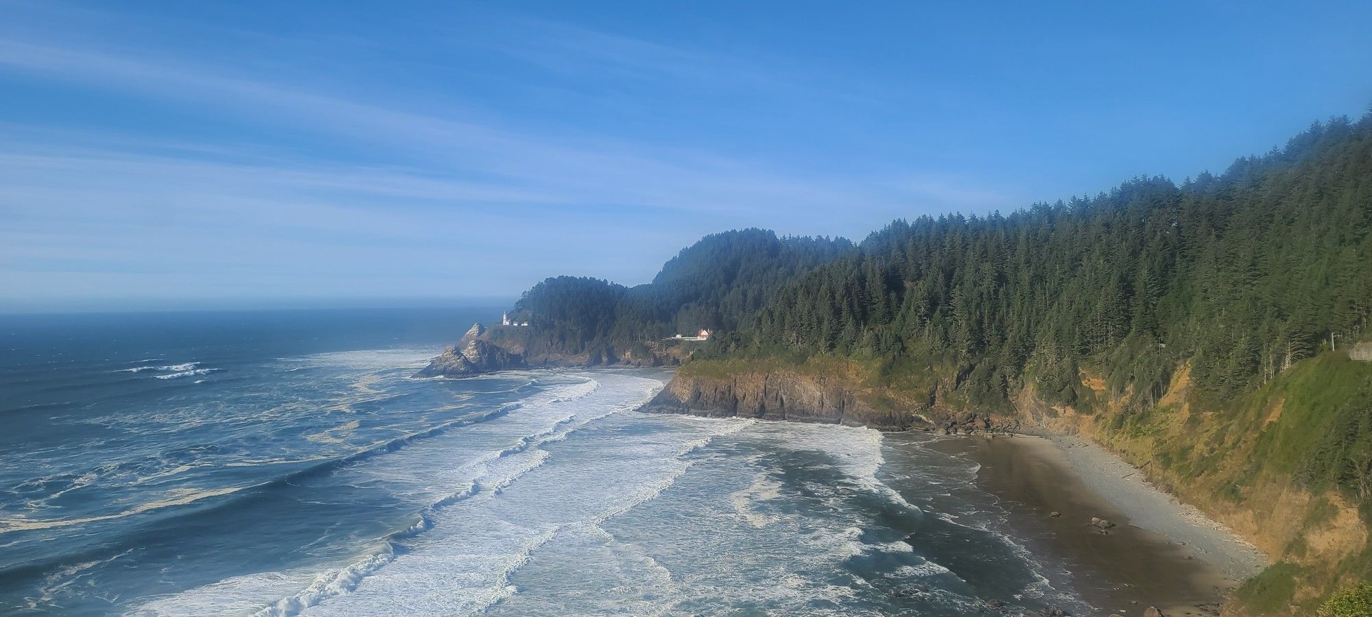 Panoramic view of ocean waves, a sandy beach, and a distant lighthouse. - Oregon Coast Scenic Bikeway