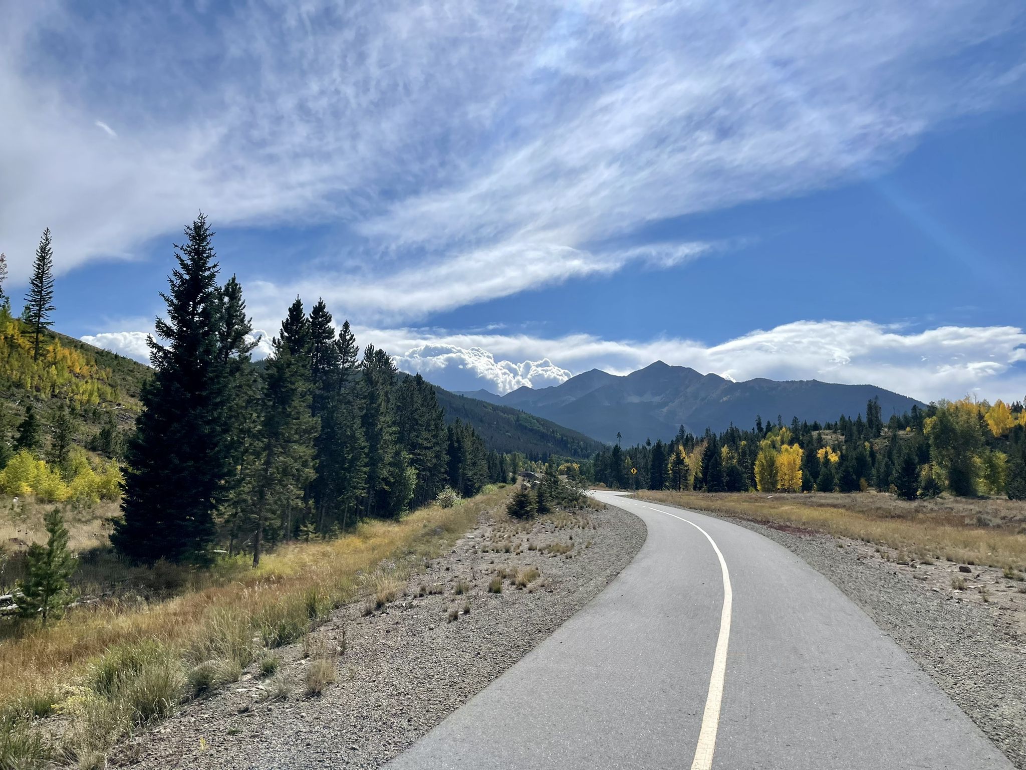 Paved road winding through evergreen and golden autumn trees with distant mountains. - View of Dillon Reservoir – Copper Mountain loop from Passage Point