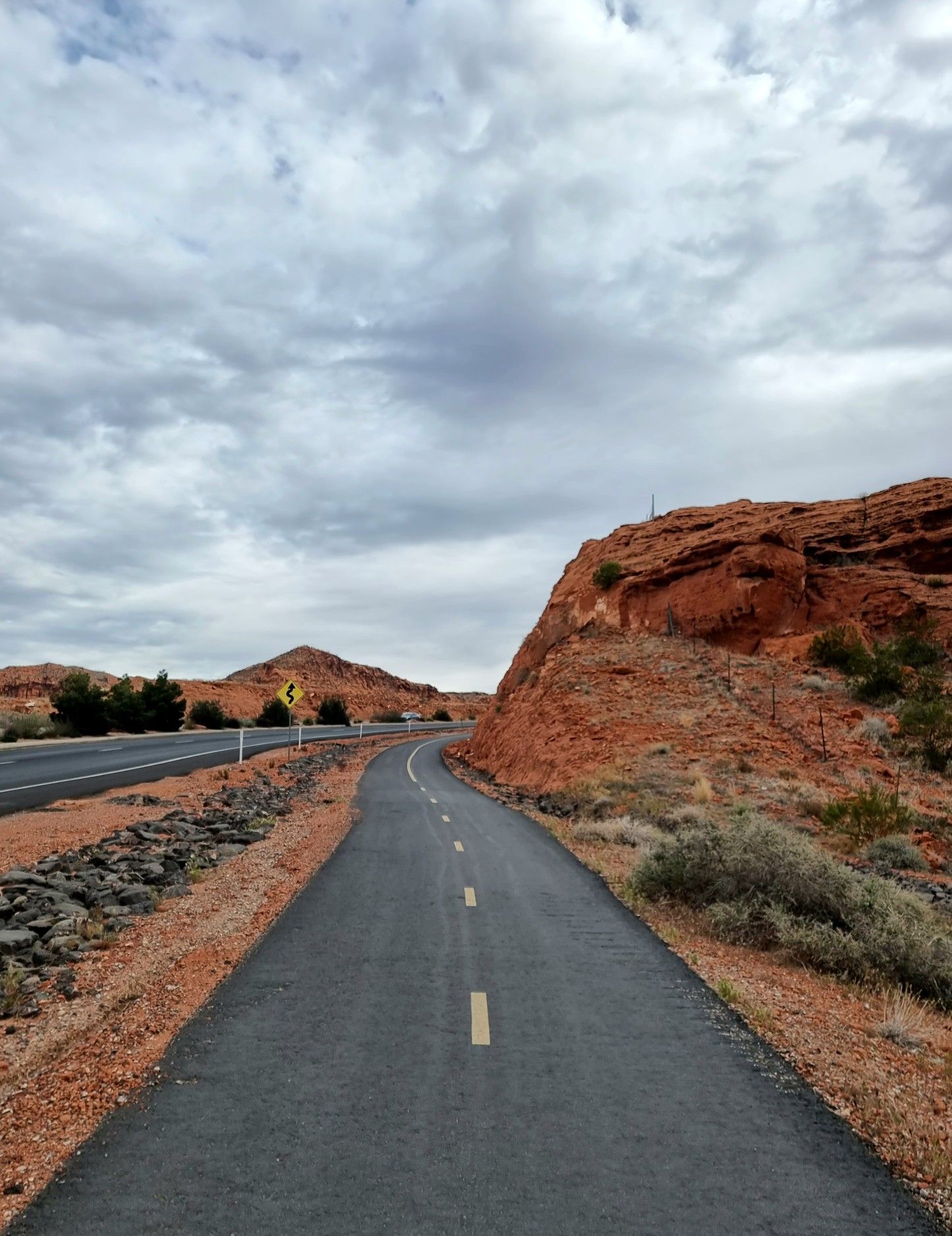 Paved path winding past red rock formations under a cloudy sky. - Chuckwalla Bike Path – Paved Bike Path loop from Washington
