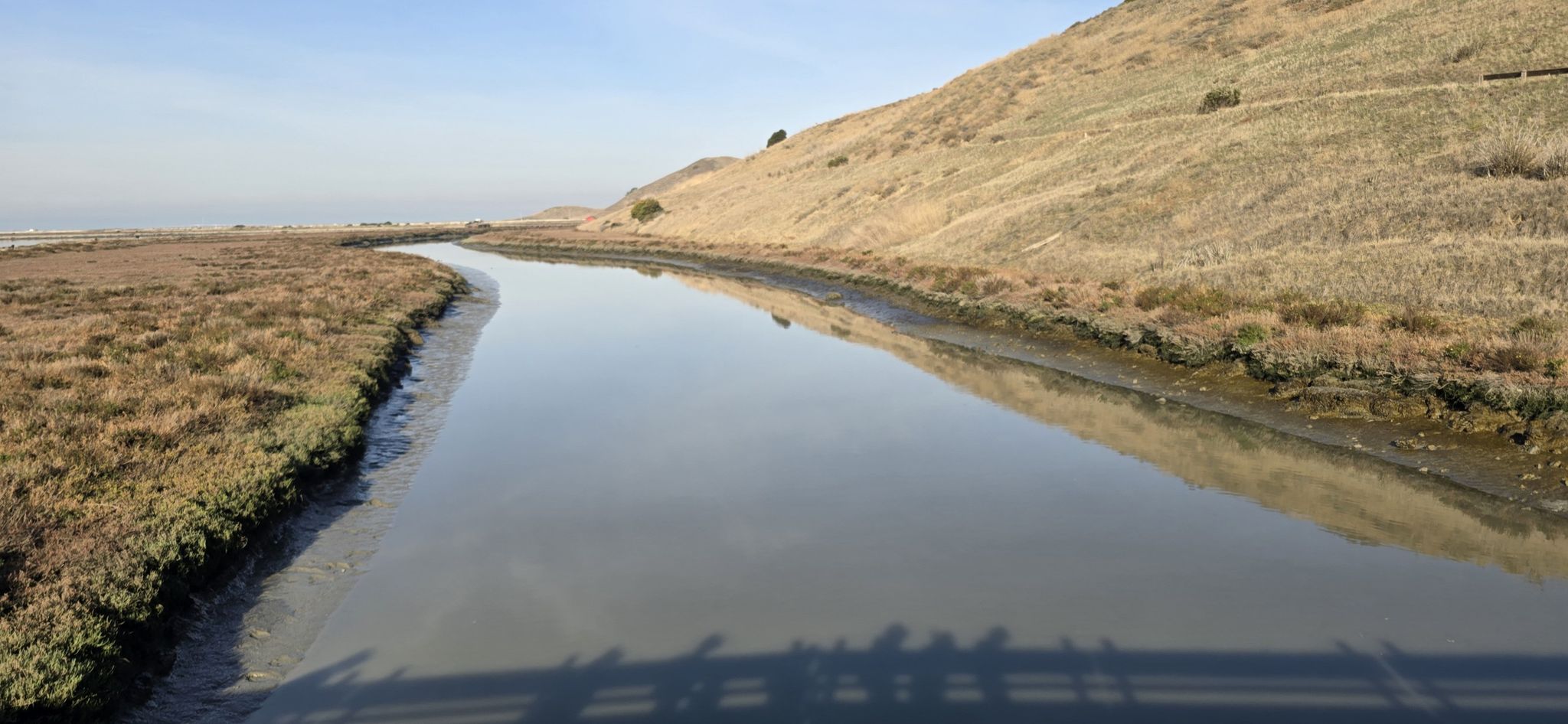 A calm river flows between a grassy bank and a dry hillside. - Newark Slough Trail