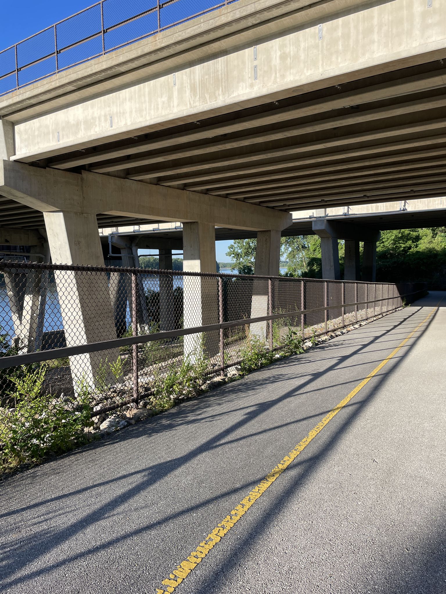A paved path with a yellow line under a concrete highway overpass. - Frontier Park – View of the Missouri River loop from Saint Charles