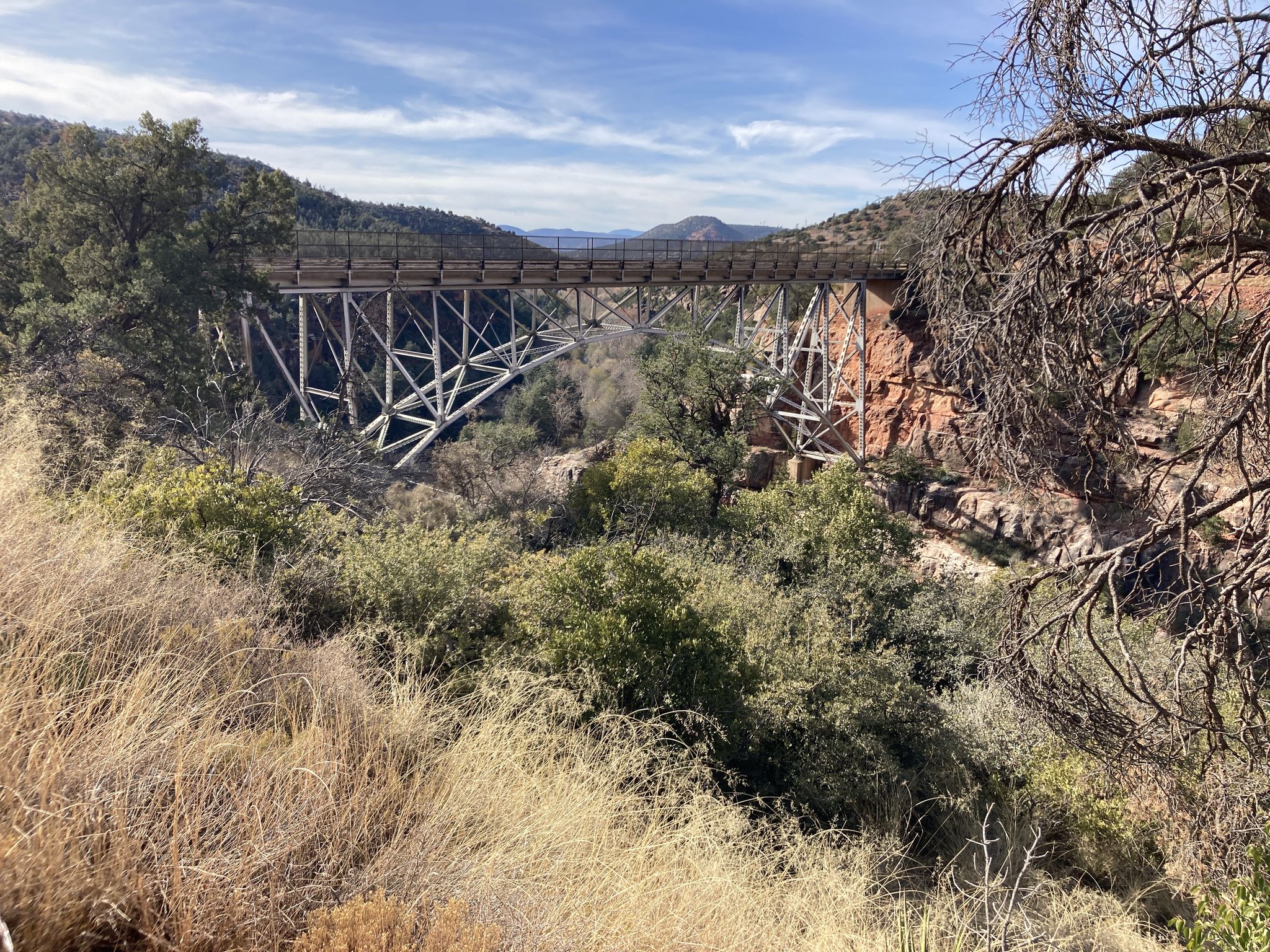 A large metal bridge spanning a canyon, surrounded by dry brush and trees. - Oak Creek Canyon Scenic Drive