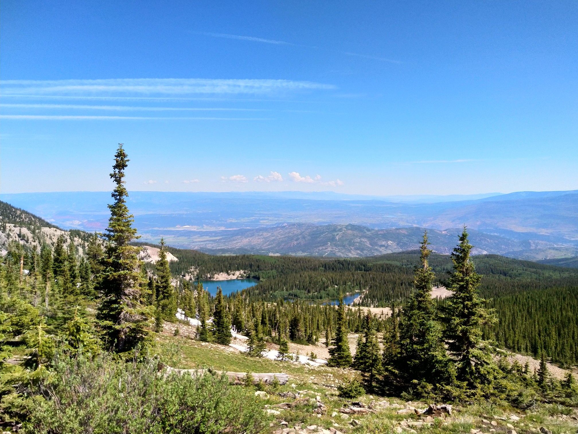 Sunny mountain view with evergreen trees, two blue lakes, and distant valleys. - Mount Sopris Trail