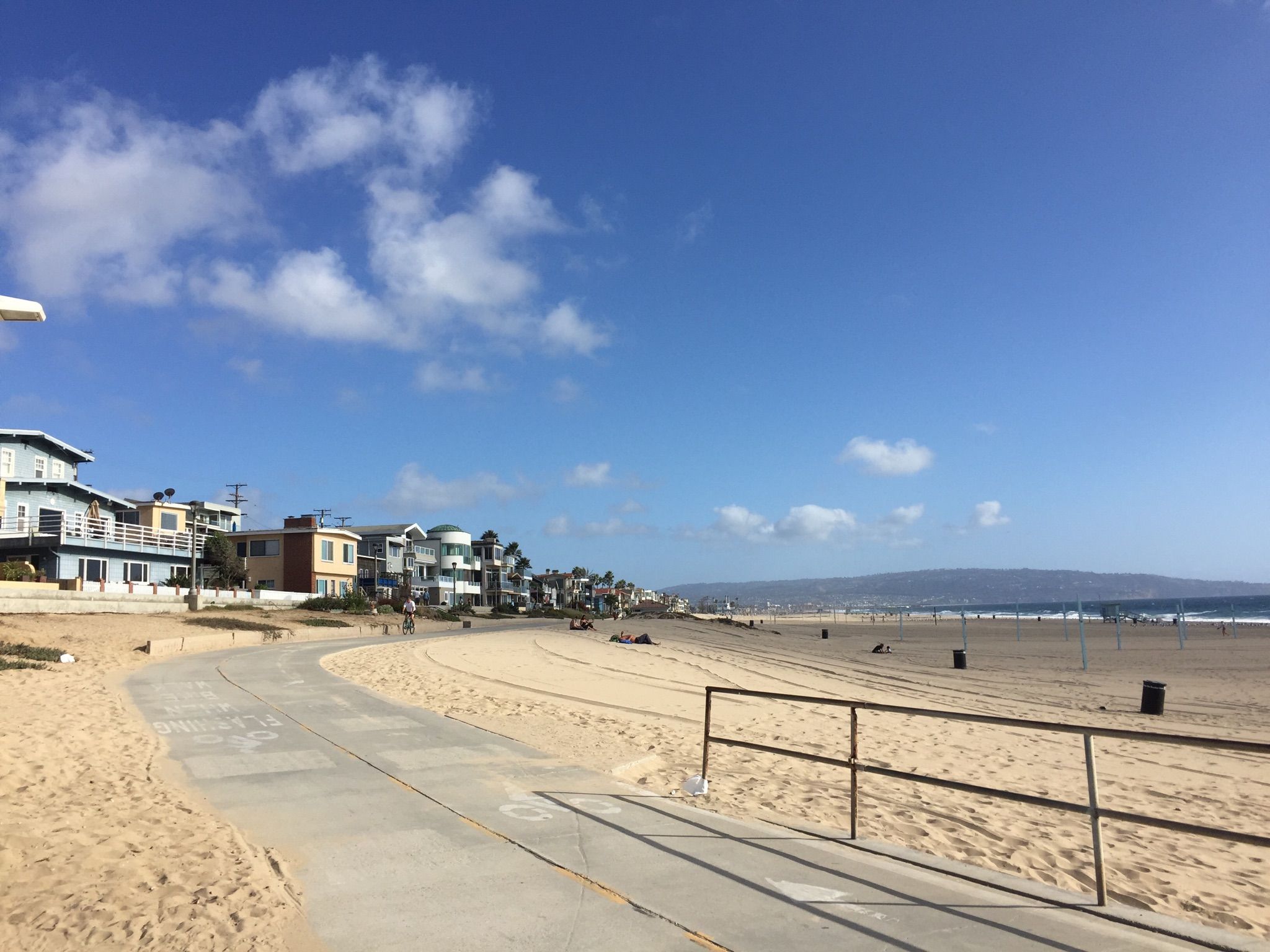 Concrete path alongside a sunny sandy beach with houses and distant hills. - Noble Park – Manhattan Beach and Pier loop from Manhattan Beach
