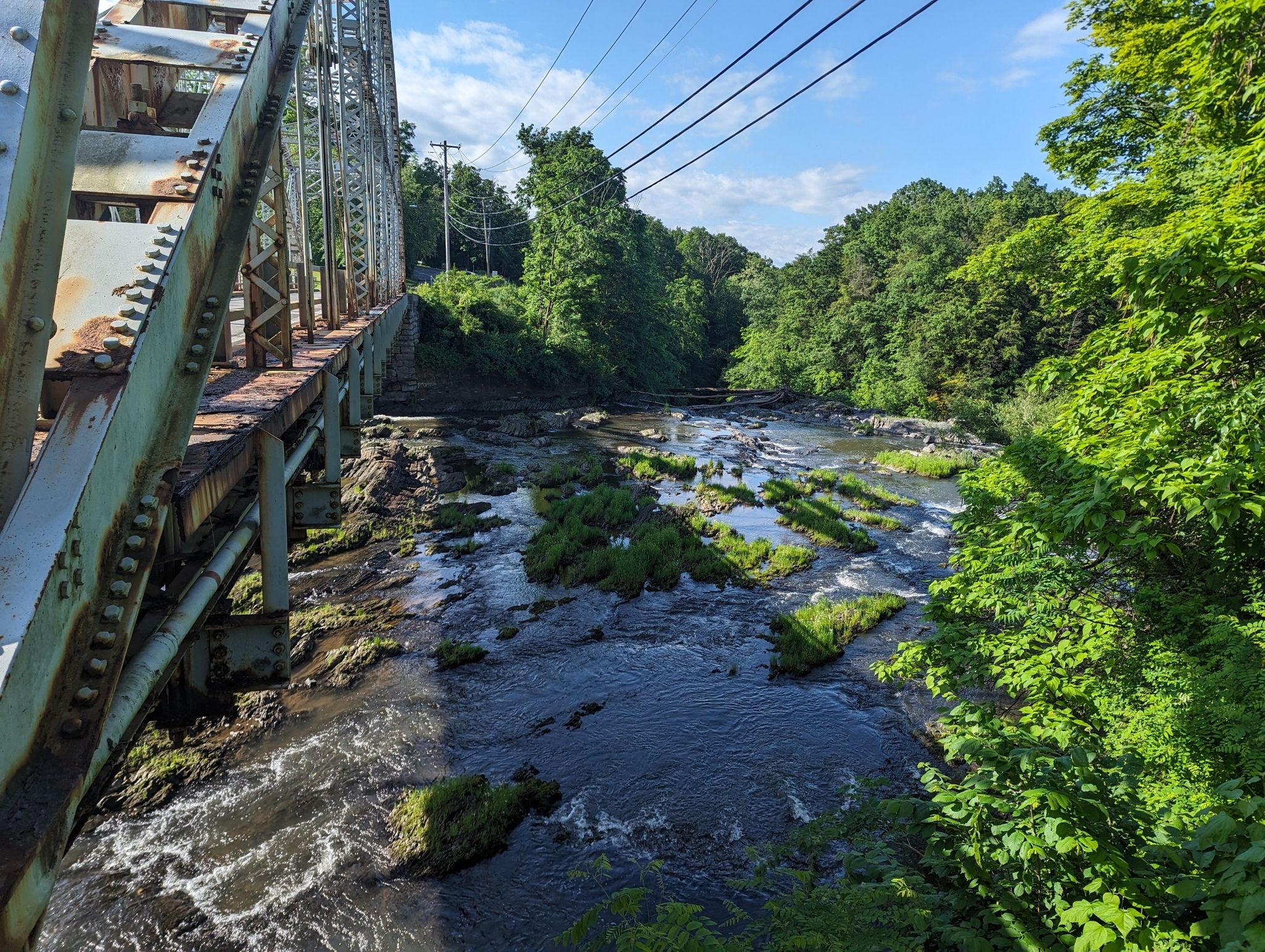 Rushing river under a metal bridge, surrounded by dense green summer trees. - Parade Hill loop from Hudson