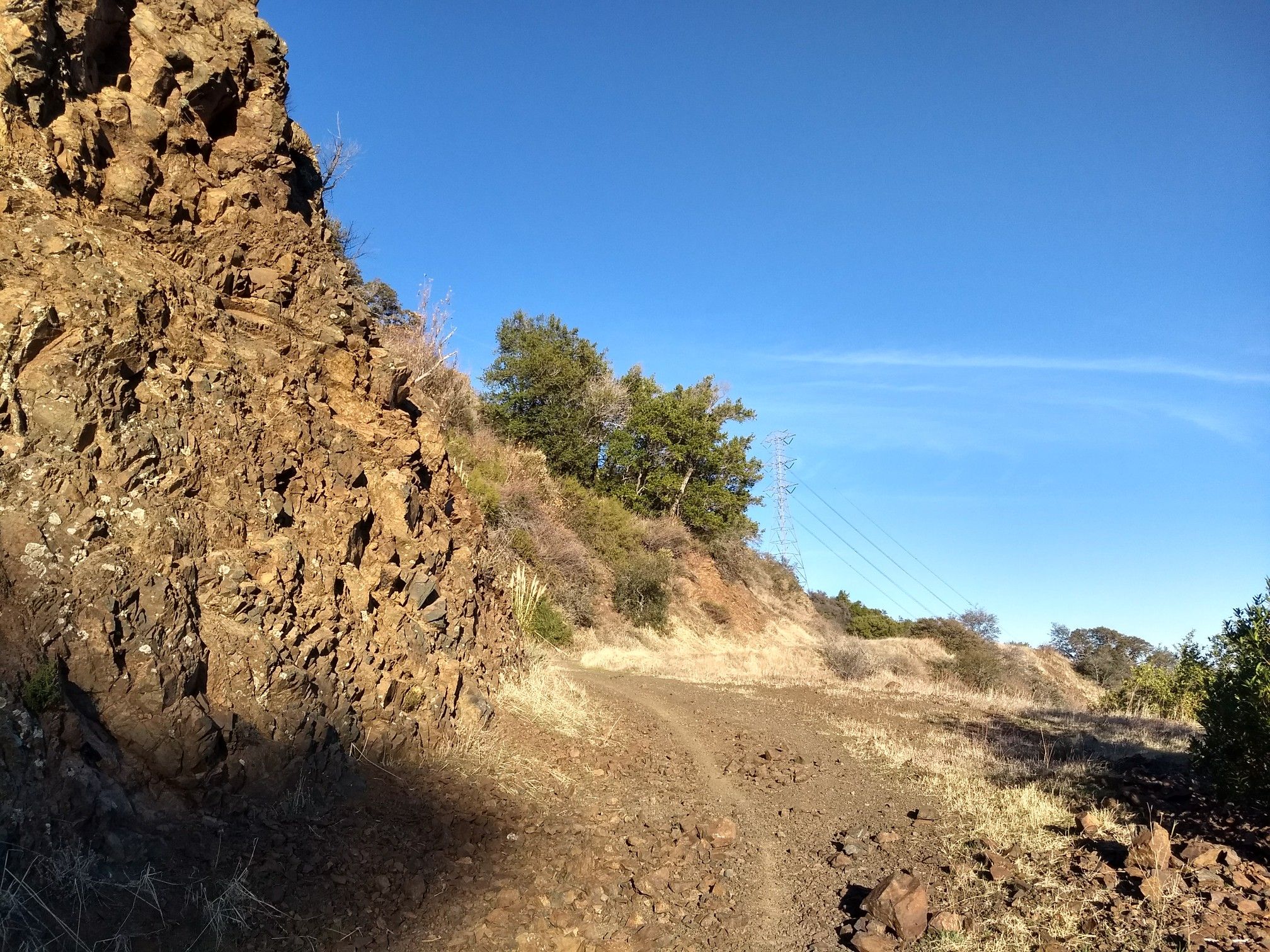 Rocky hillside next to a dirt path under a clear blue sky. - Mount El Sombroso via Woods Trail