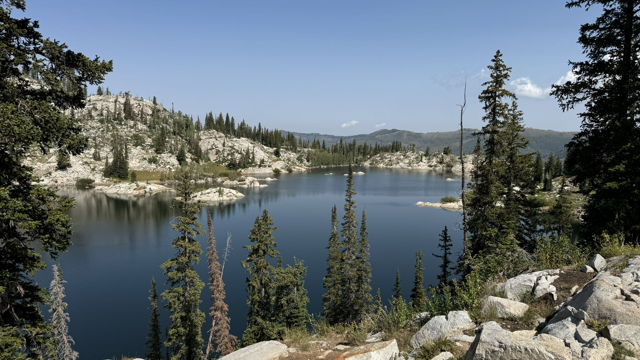 Bright daylight on a mountain lake with rocky shores and green pine trees. - Lake Catherine via Brighton Lakes Trail