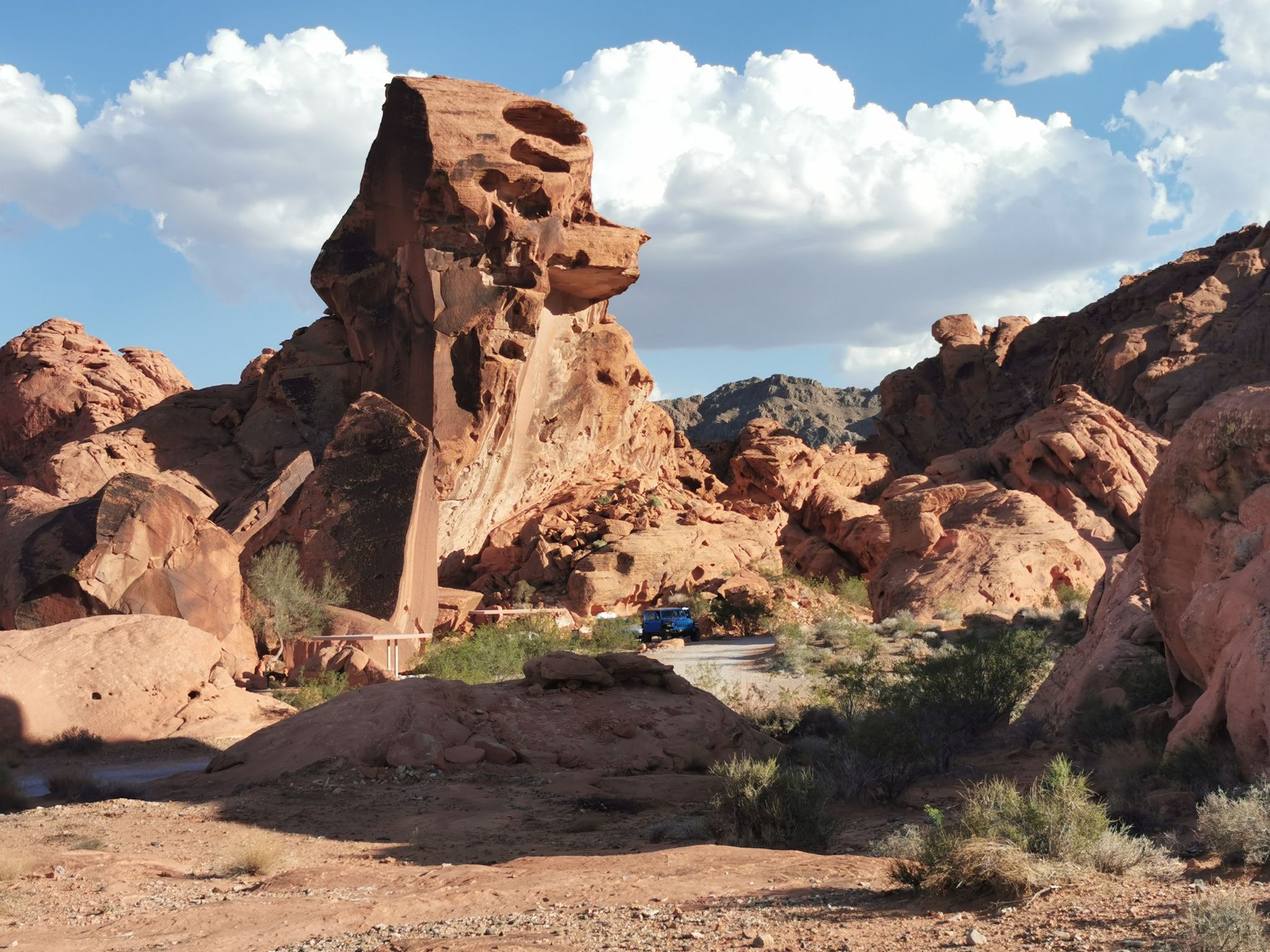 Massive red rock formations, a road, and a blue vehicle under a cloudy sky. - Arch Rock, Beehives, and Petrified Logs loop