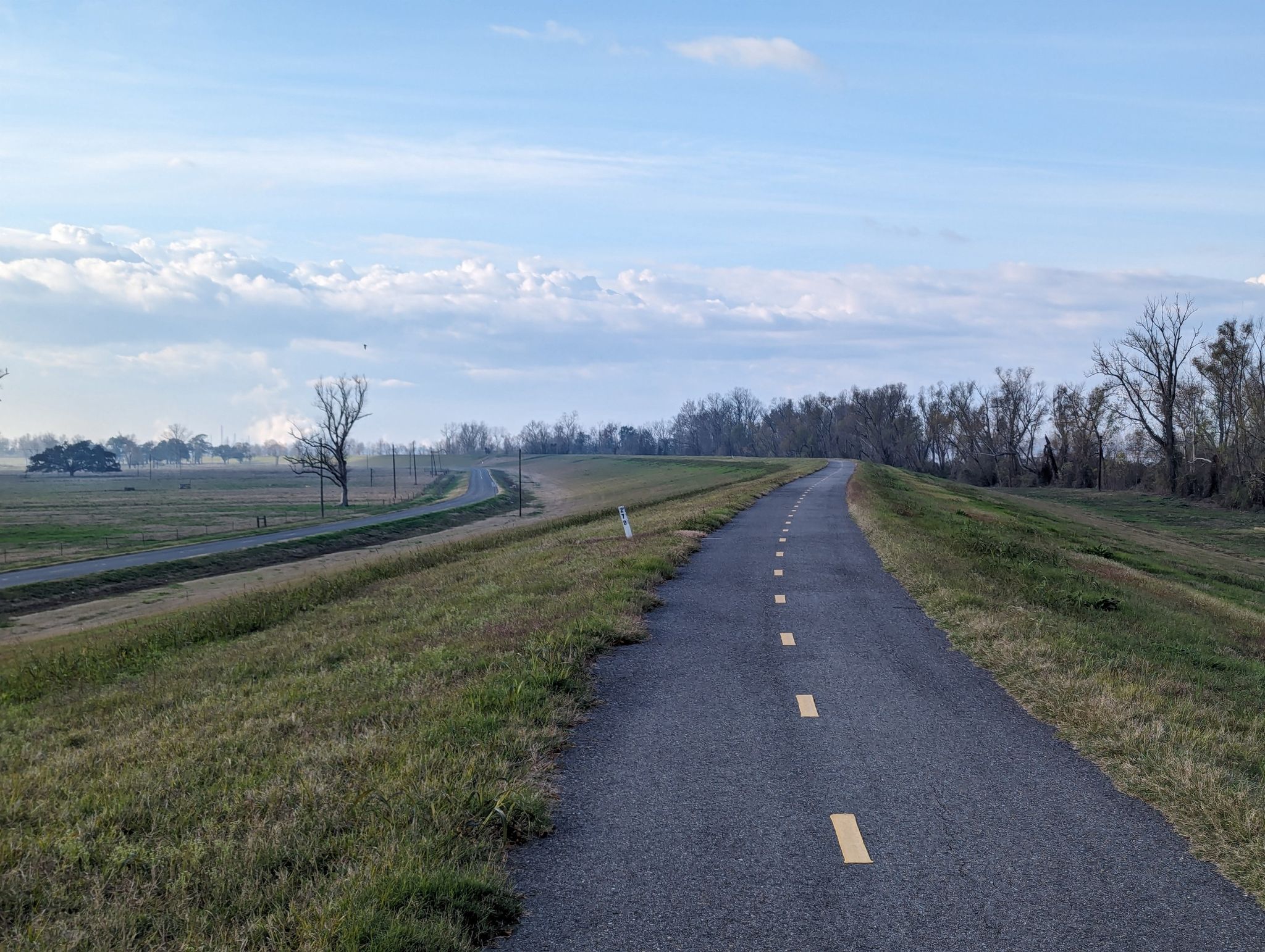 Paved road with yellow lines on a grassy embankment under a cloudy sky. - Mississippi River Levee Trail loop from Farr Park Equestrian Center and RV Campground
