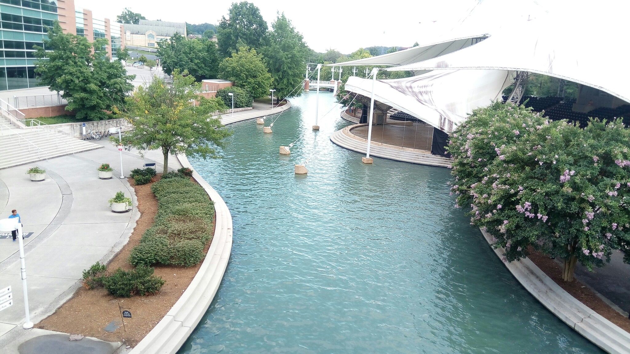 Urban canal with modern buildings, trees, and a large white canopy structure. - UT/Downtown to and from West Hills and Cedar Bluff Areas