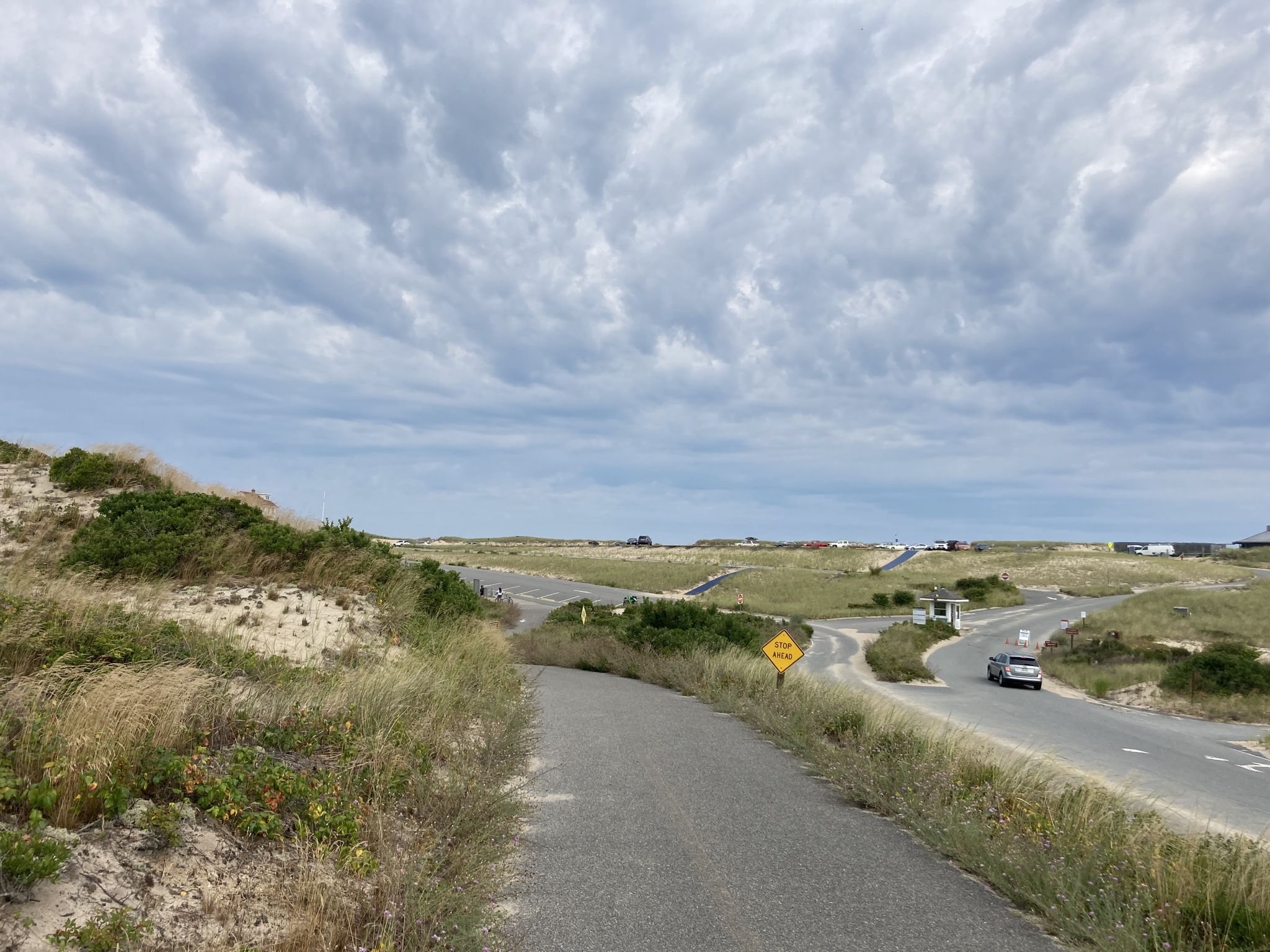 Road intersection with a car, surrounded by grassy dunes under a cloudy sky. - Cape Cod National Seashore – Province Lands Bike Trail loop from Provincetown