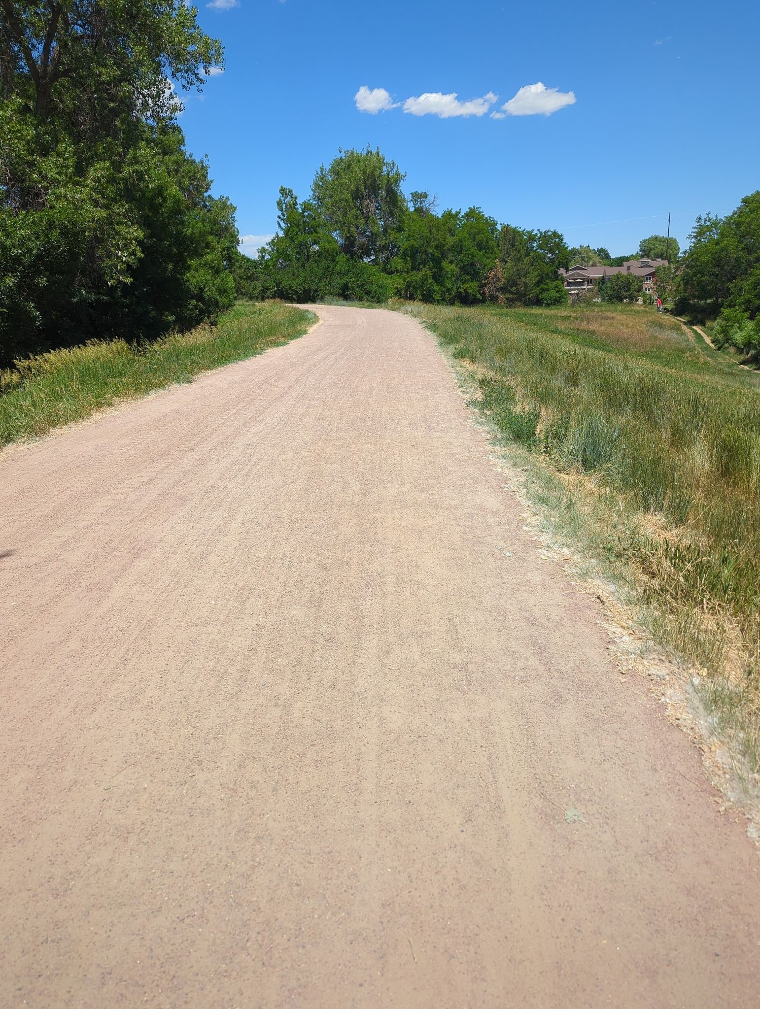 A wide dirt path curves through green grass under a bright blue sky. - deKoevend Park Trail Loop