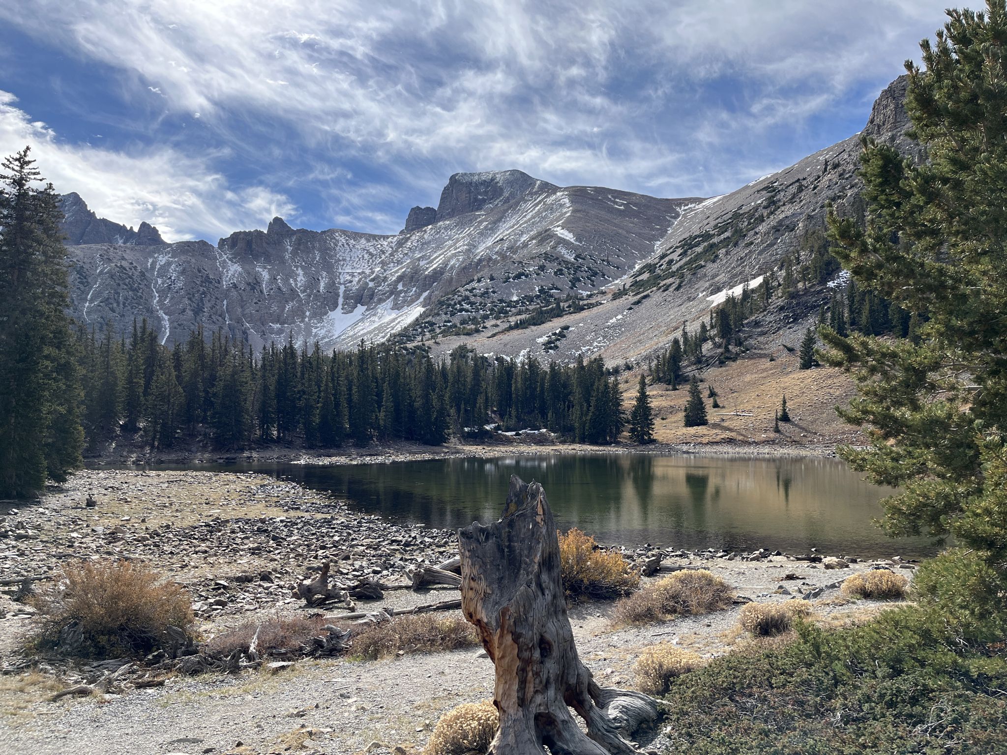 A mountain lake with pine trees and snow-dusted peaks under a cloudy sky. - Stella Lake via Alpine Lakes Loop Trail