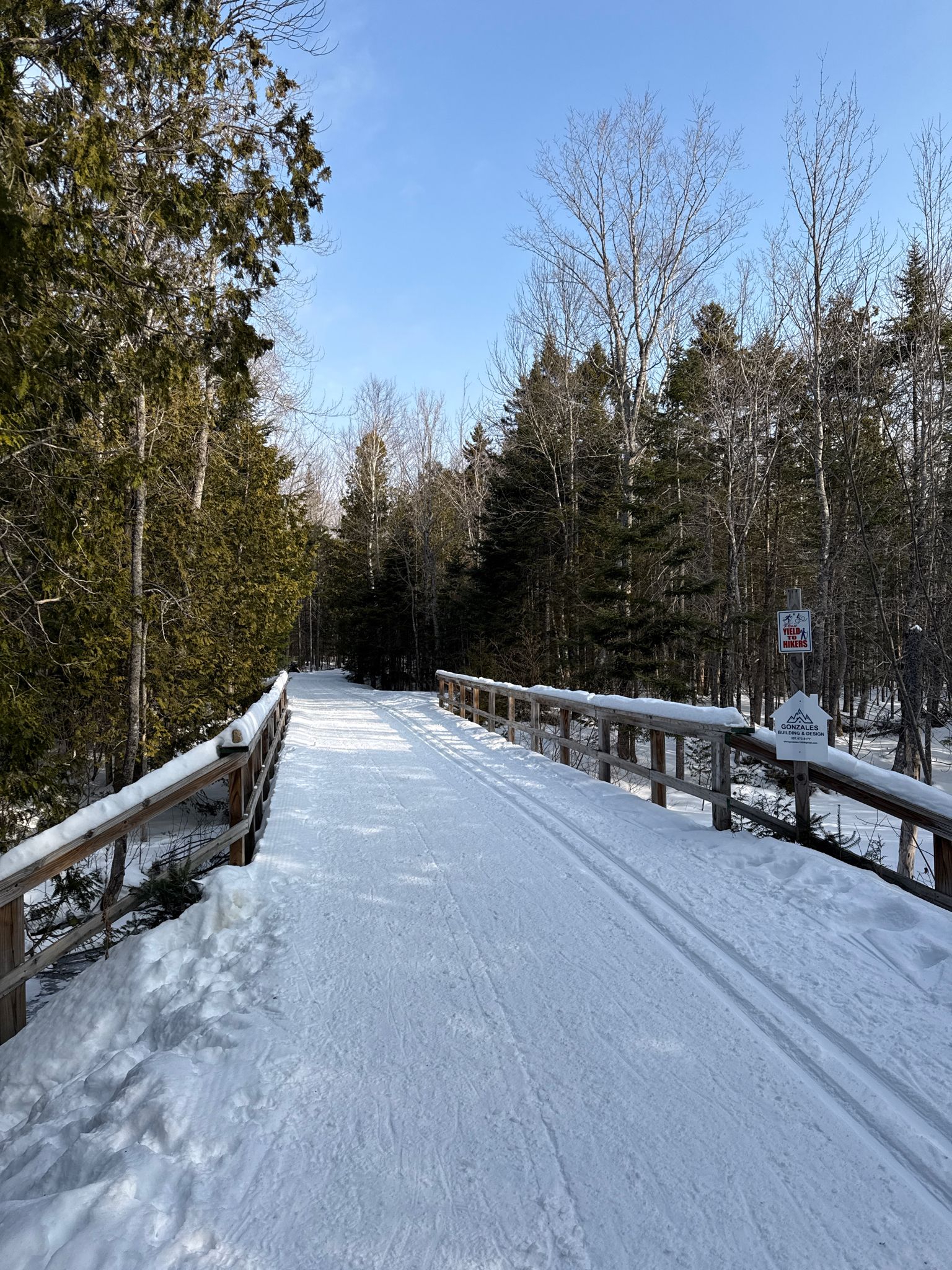 Snowy wooden bridge with ski tracks extends through a sunny winter forest. - Sugarloaf Mountain loop from Village Gated Parking