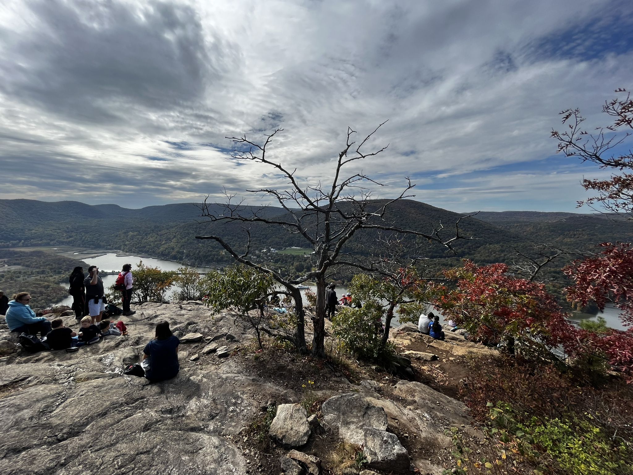 Group of people resting on a rocky overlook with a river and hills. - Anthony's Nose via Camp Smith Trail