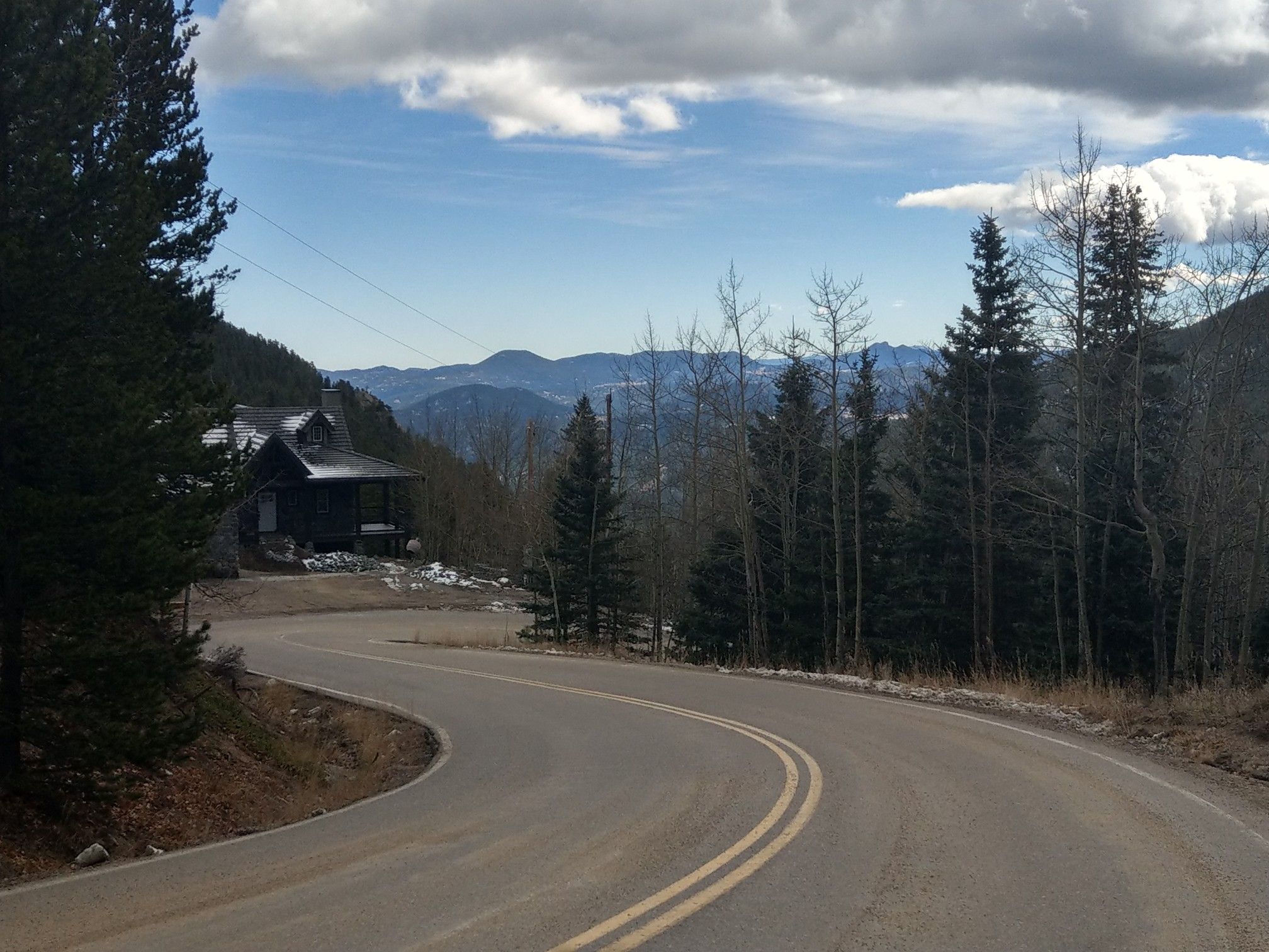 A winding road leads past a house with distant mountains under cloudy skies. - Idaho Springs to Witter Gulch — Gravel