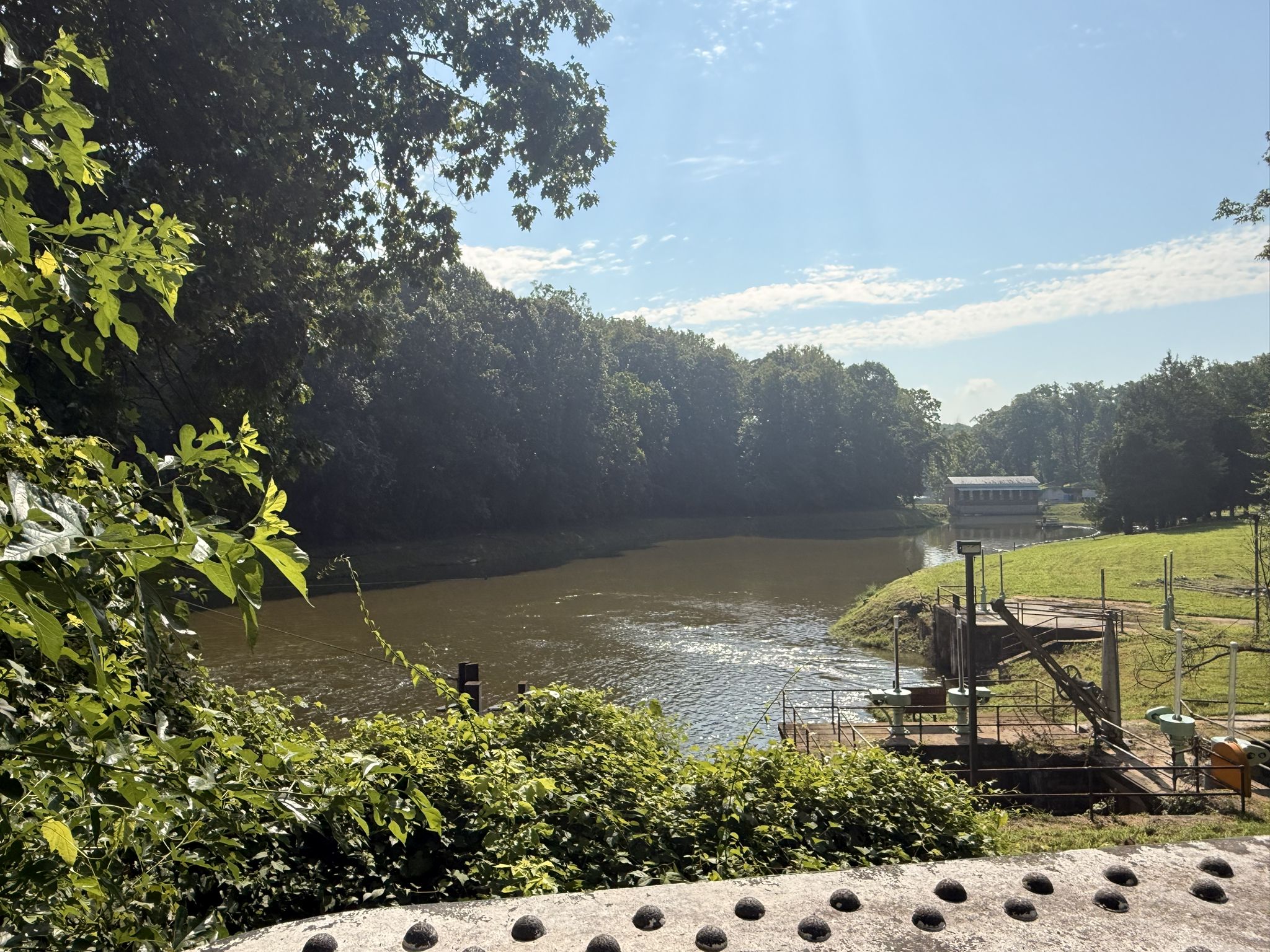 Wide river with green trees, industrial structure, and bright blue sky. - Capital Crescent and Little Falls Trail Loop