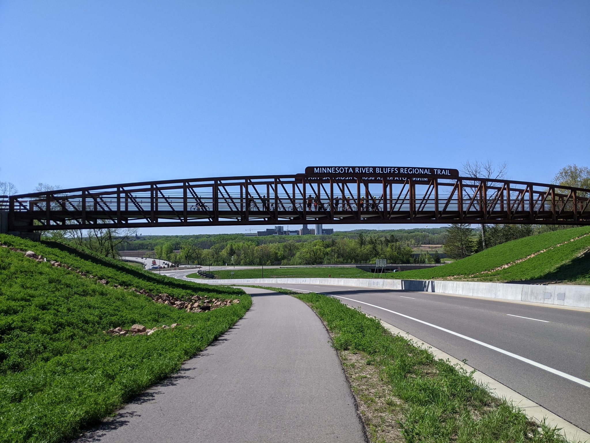 A large metal pedestrian bridge spans over a road on a sunny day. - Pioneer Trail and Flying Cloud Drive Loop