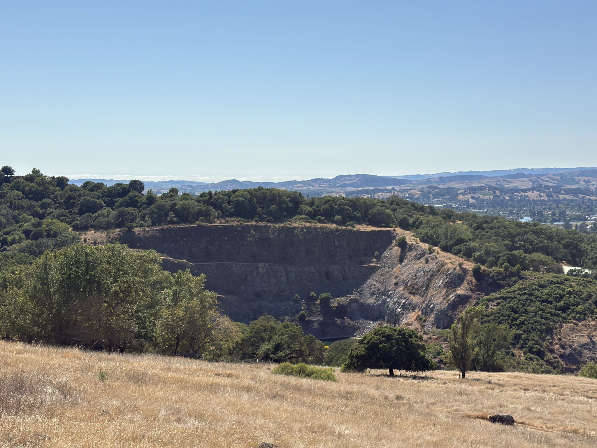 A large quarry cut into a hillside, surrounded by trees and dry grass under a clear sky. - Lake Marie – Skyline Ridge Trail loop from Napa State Hospital