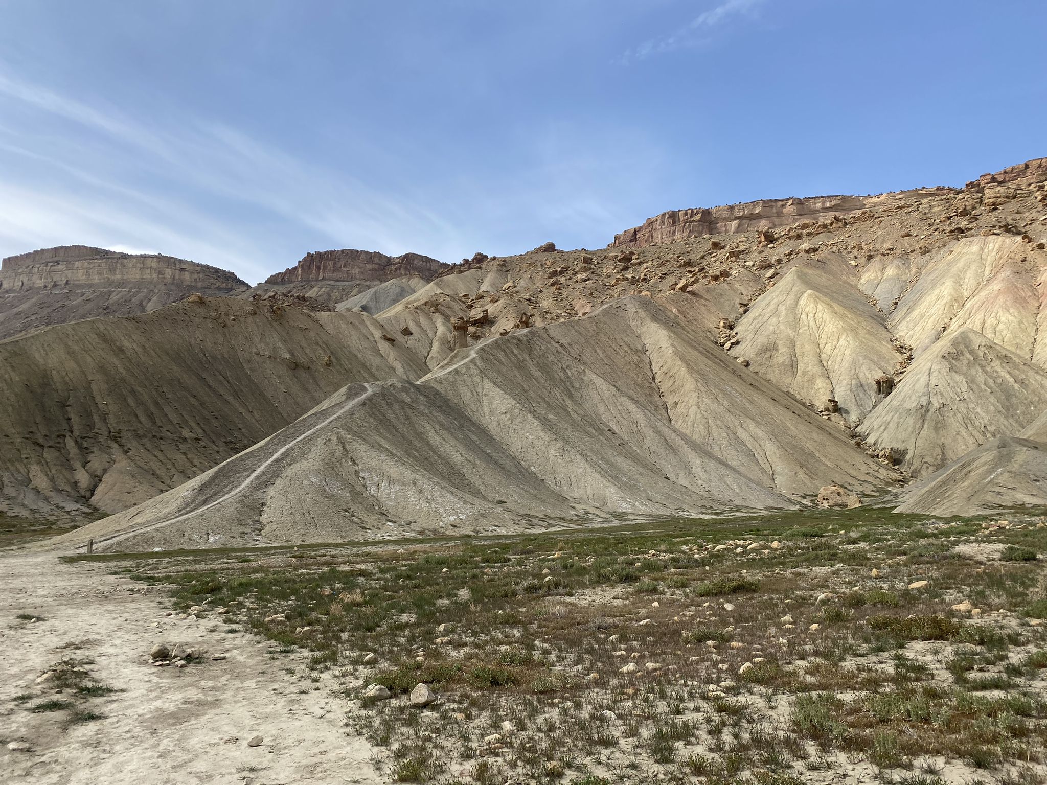 Eroded hillsides and towering cliffs under a bright, partly cloudy sky. - Mount Garfield Trail