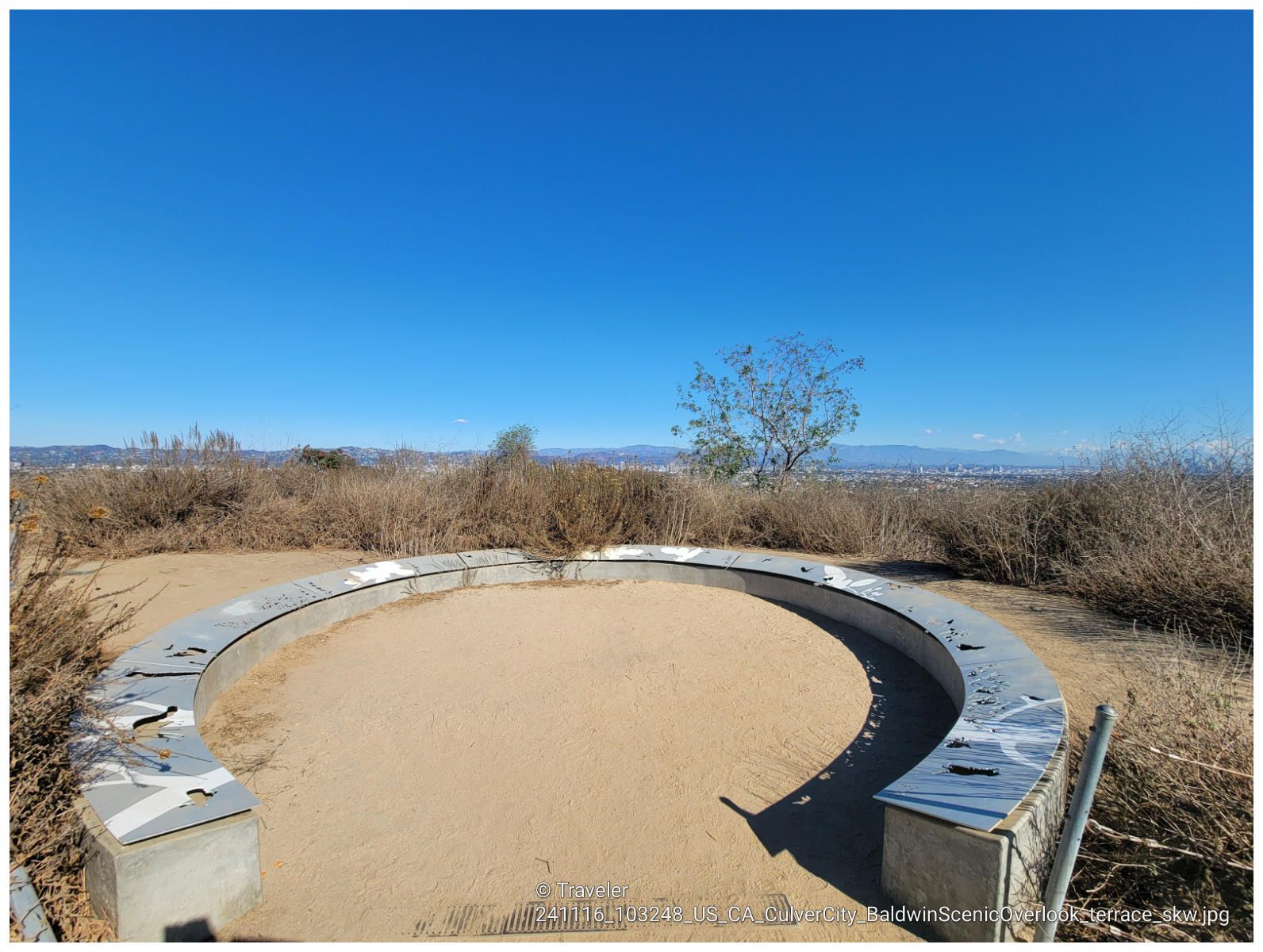 A circular sandy area with a concrete bench under a clear blue sky. - Hillside Trail