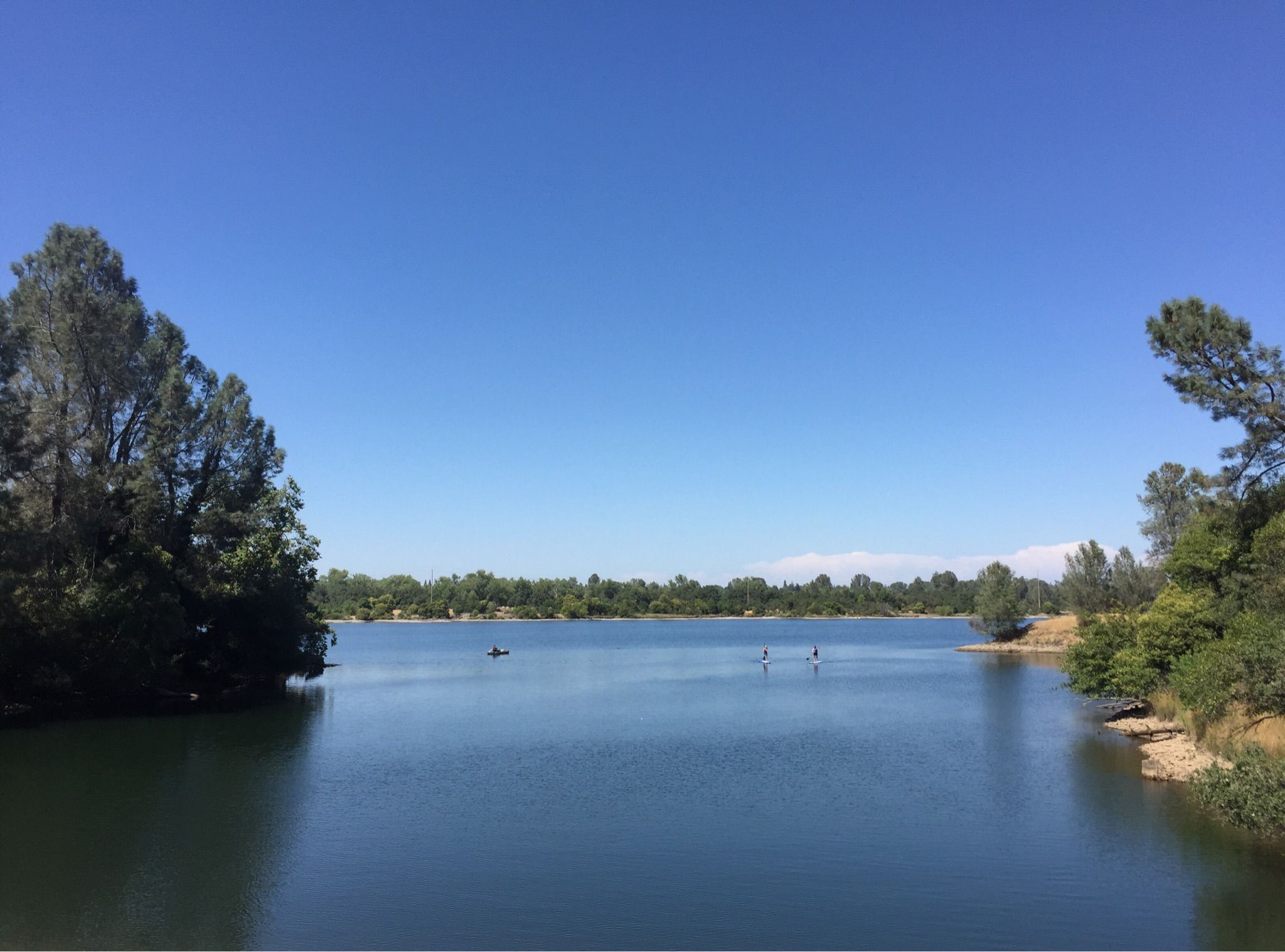 A wide blue lake with distant kayakers and paddleboarders under a clear sky. - Lake Natoma – Folsom Historic Truss Bridge loop from Iron Point