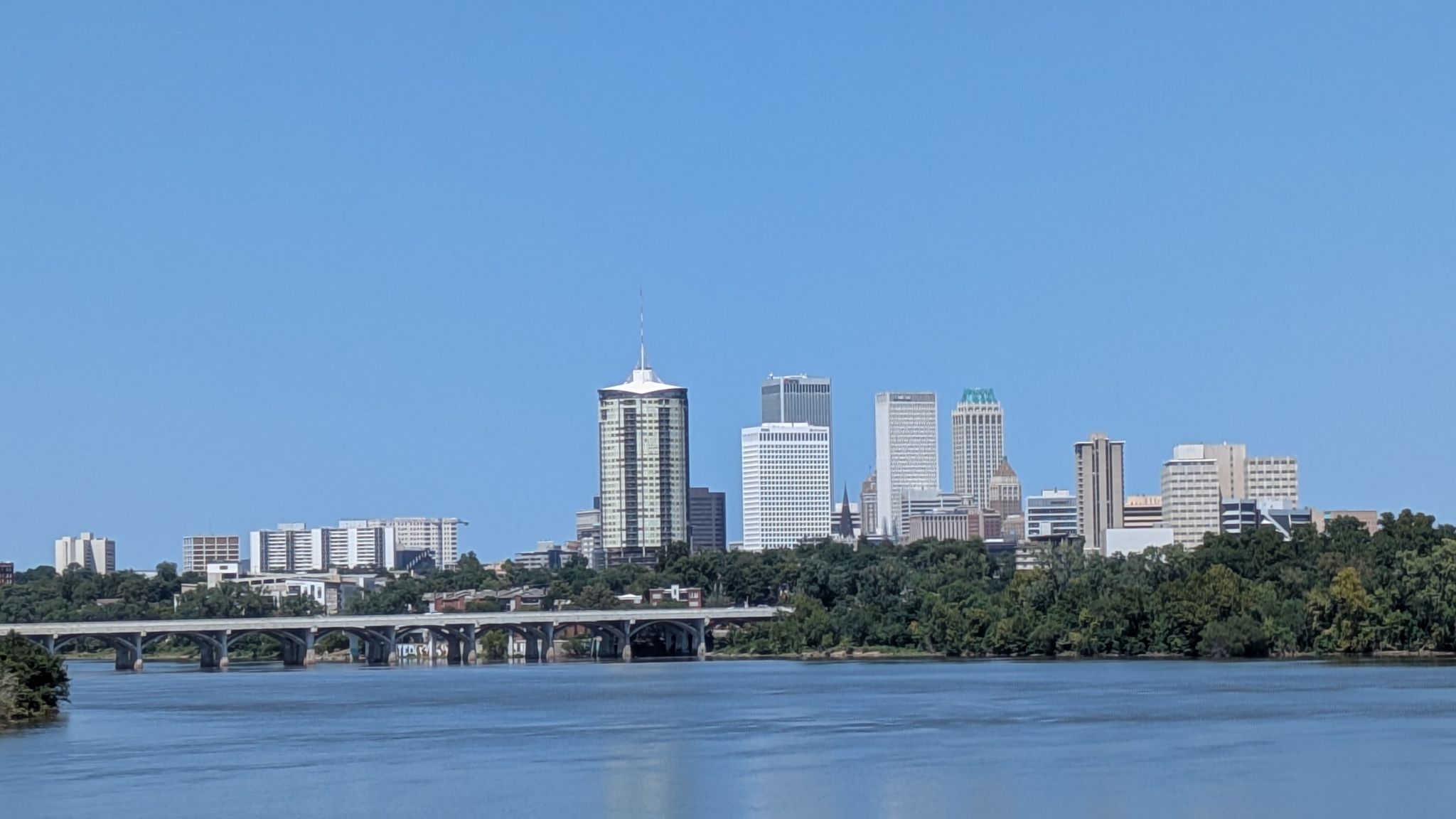 City skyline with tall buildings visible across a wide river and green trees. - The Gathering Place – Gathering Place Park loop from Philbrook Museum of Art