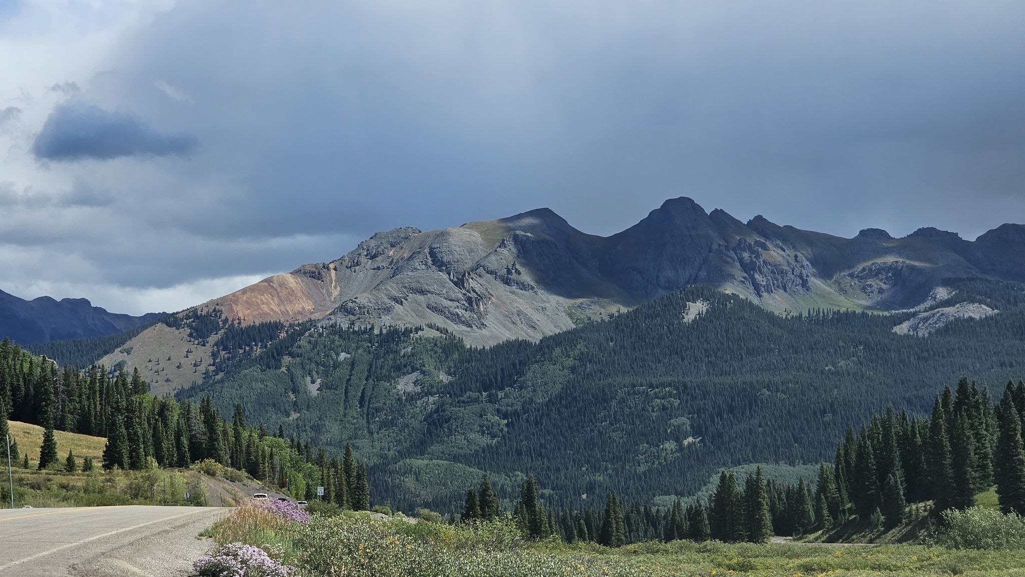 Paved road leading towards rugged mountains and evergreen forests under dramatic clouds. - Telluride to Lizard Head Pass