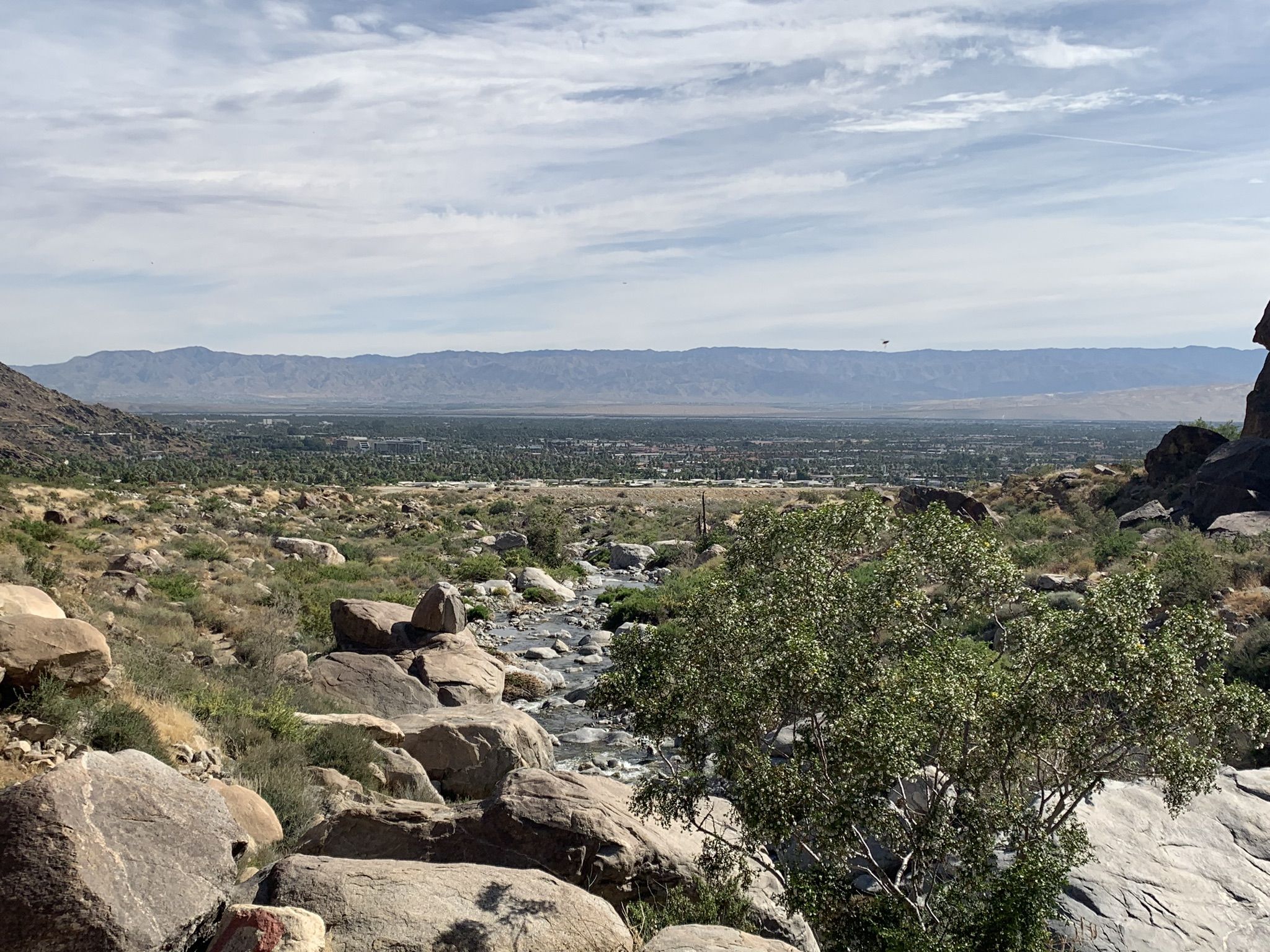 Wide view of a green valley and distant mountains under a partly cloudy sky. - Tahquitz Canyon Trail
